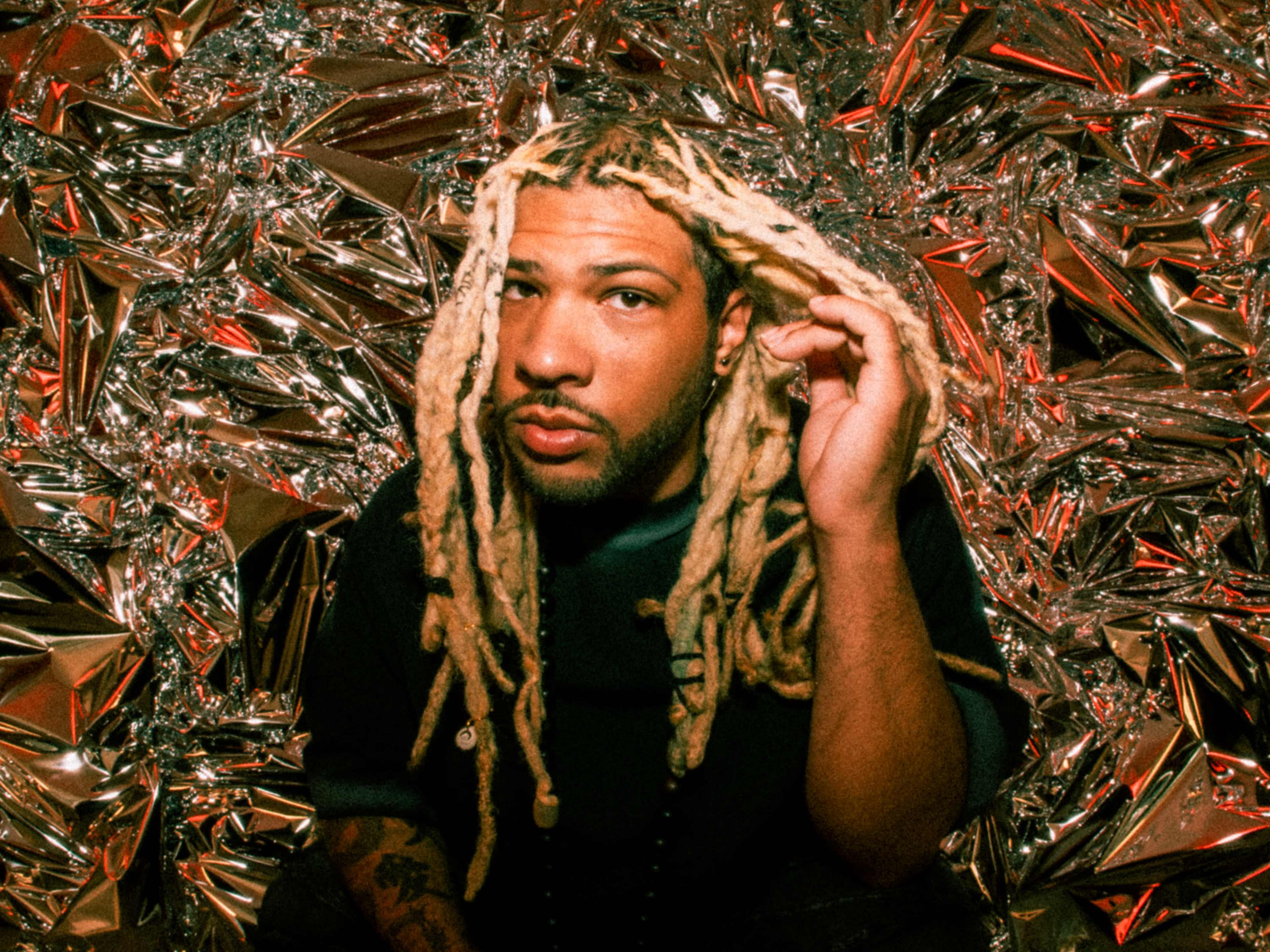 A person with long, styled hair is posing in front of a shiny, crinkled metallic background.