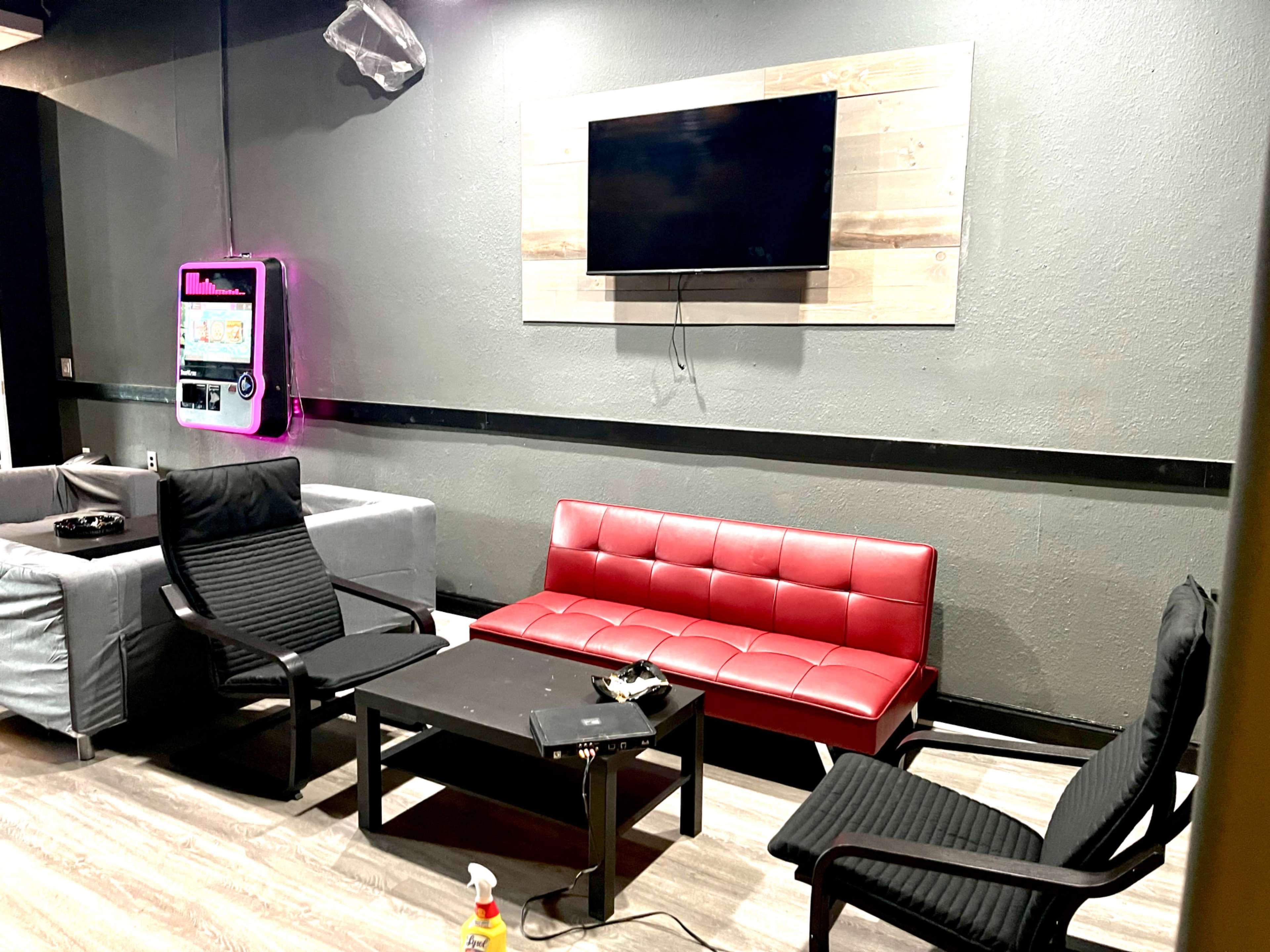The image shows a lounge area with a red couch, several black chairs, a table, and a wall-mounted television.