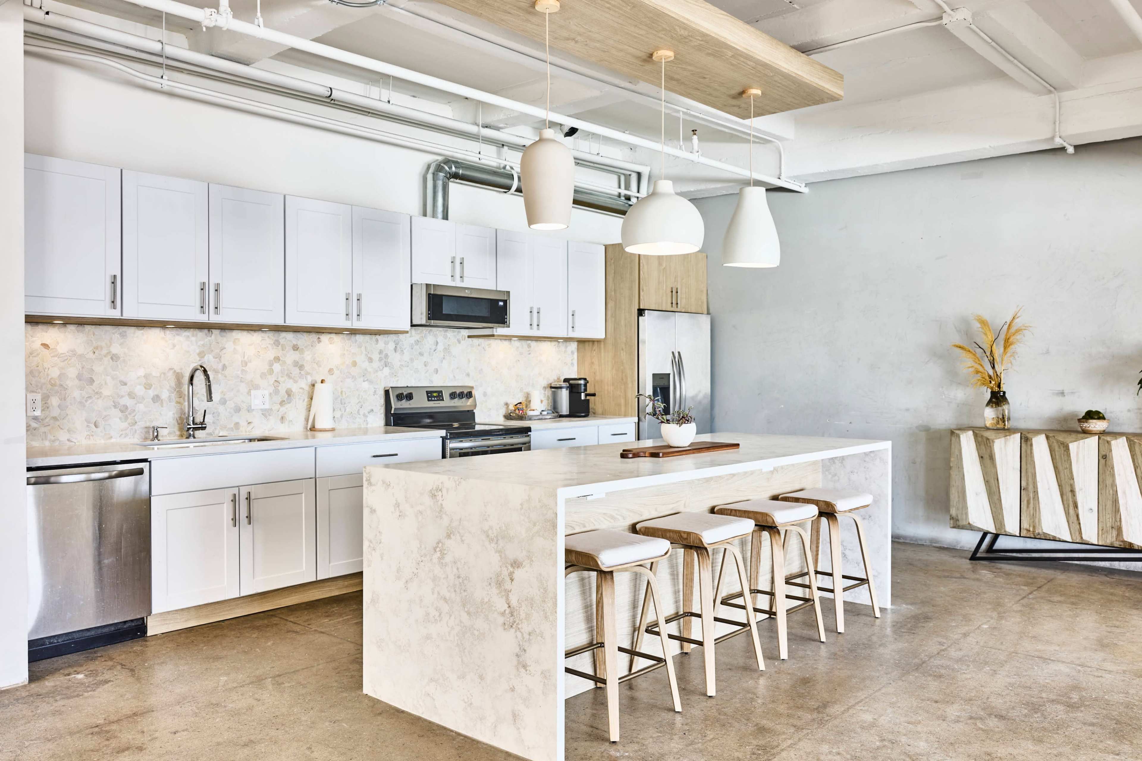 The image shows a modern kitchen with white cabinetry, a large island with bar stools, and a combination of stainless steel and wood appliances.