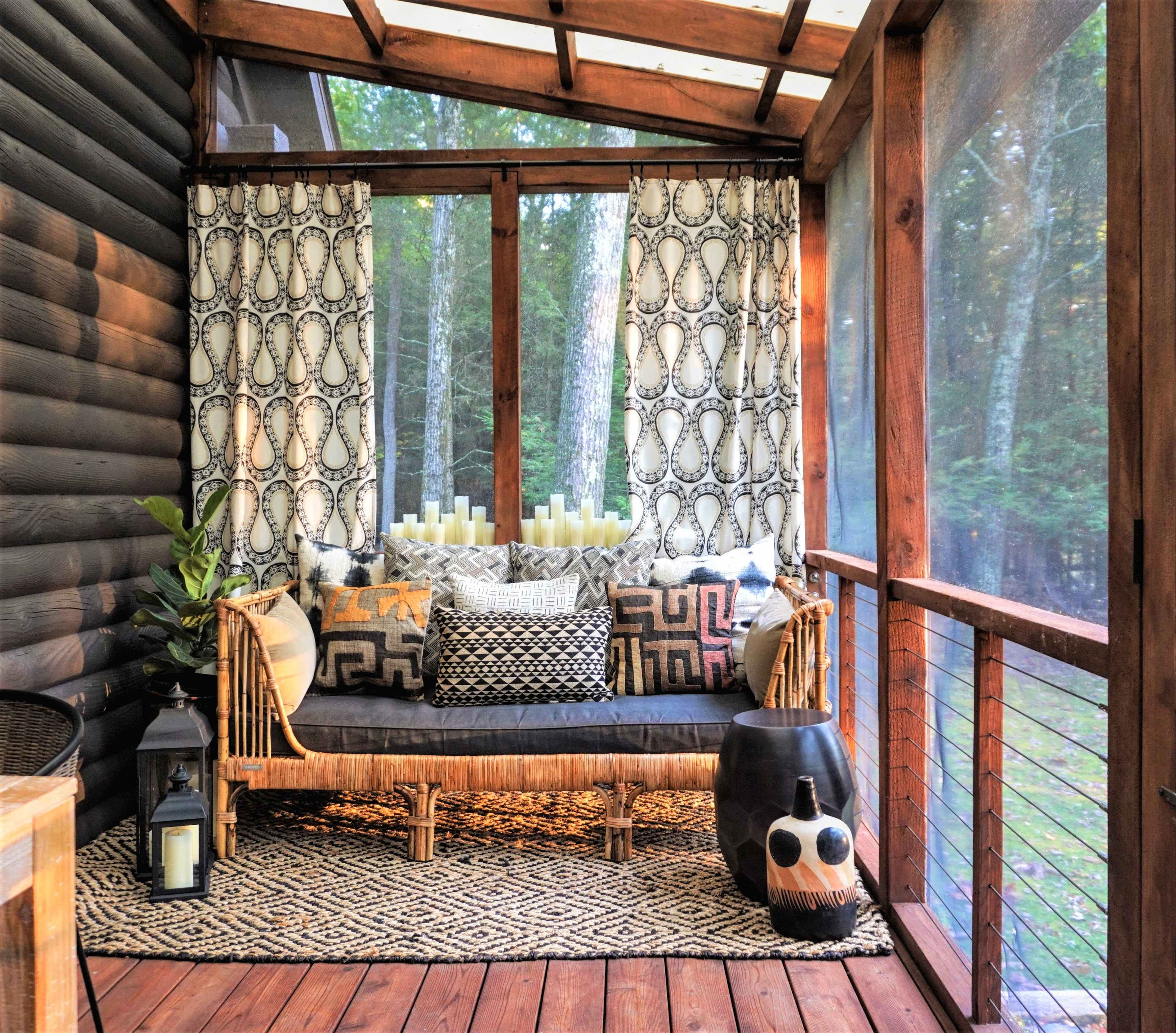 A cozy porch features a bamboo sofa adorned with patterned cushions, surrounded by decorative curtains and a collection of candles on a wooden table.