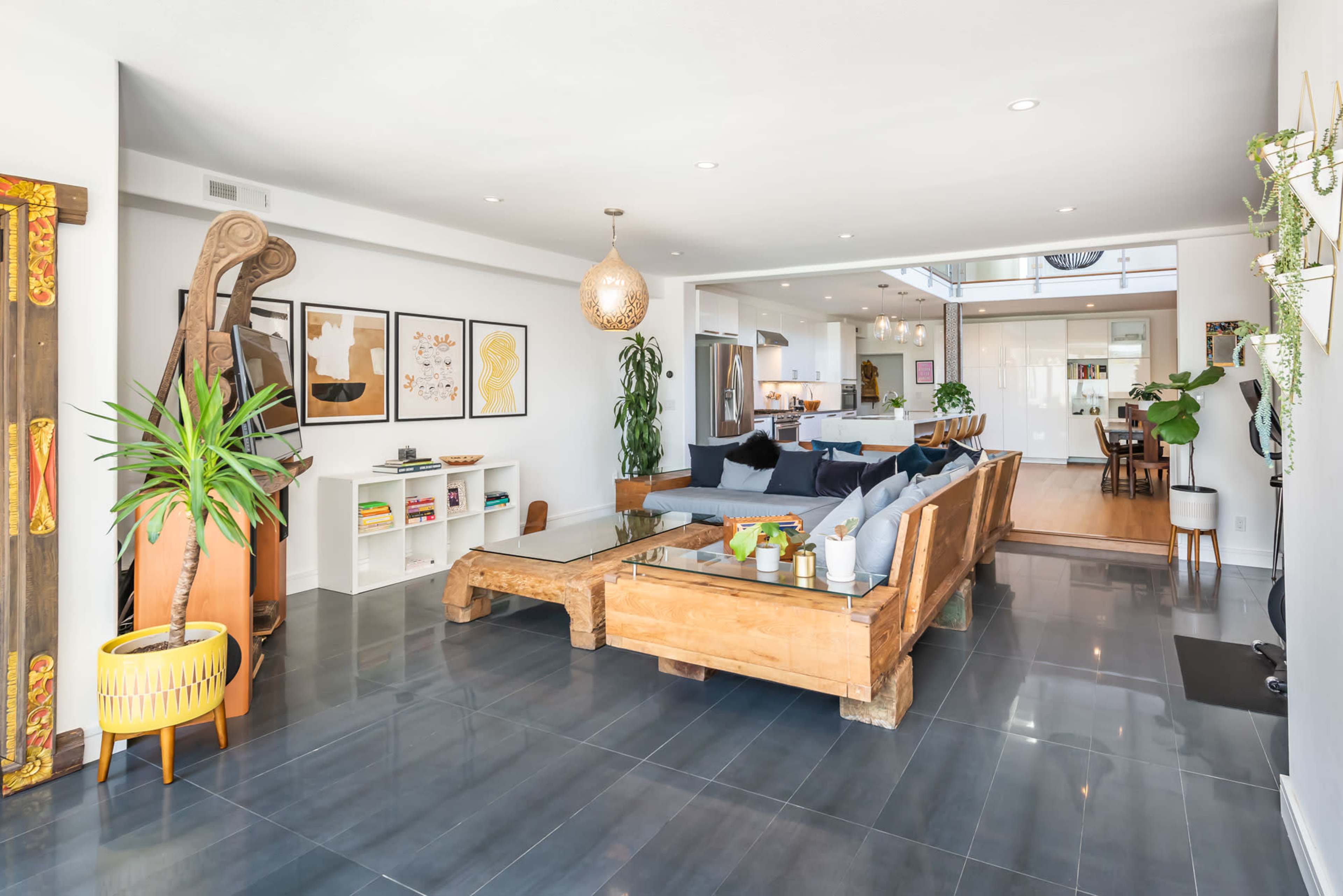 A spacious living room with a wooden seating arrangement, large artwork on the walls, and a view into a modern kitchen.