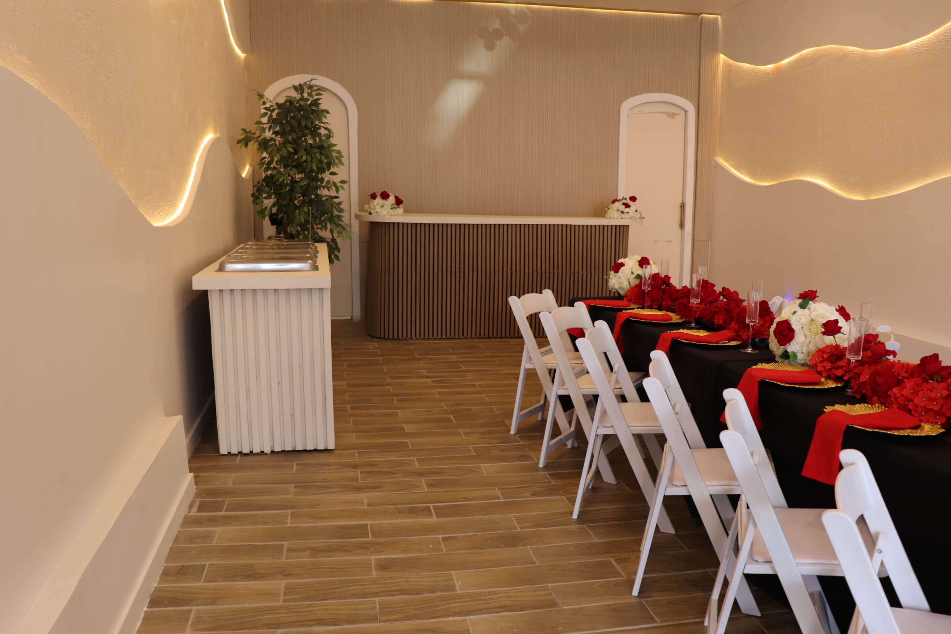 The image shows an elegantly arranged dining area with white chairs and a black table set with red and white floral centerpieces.