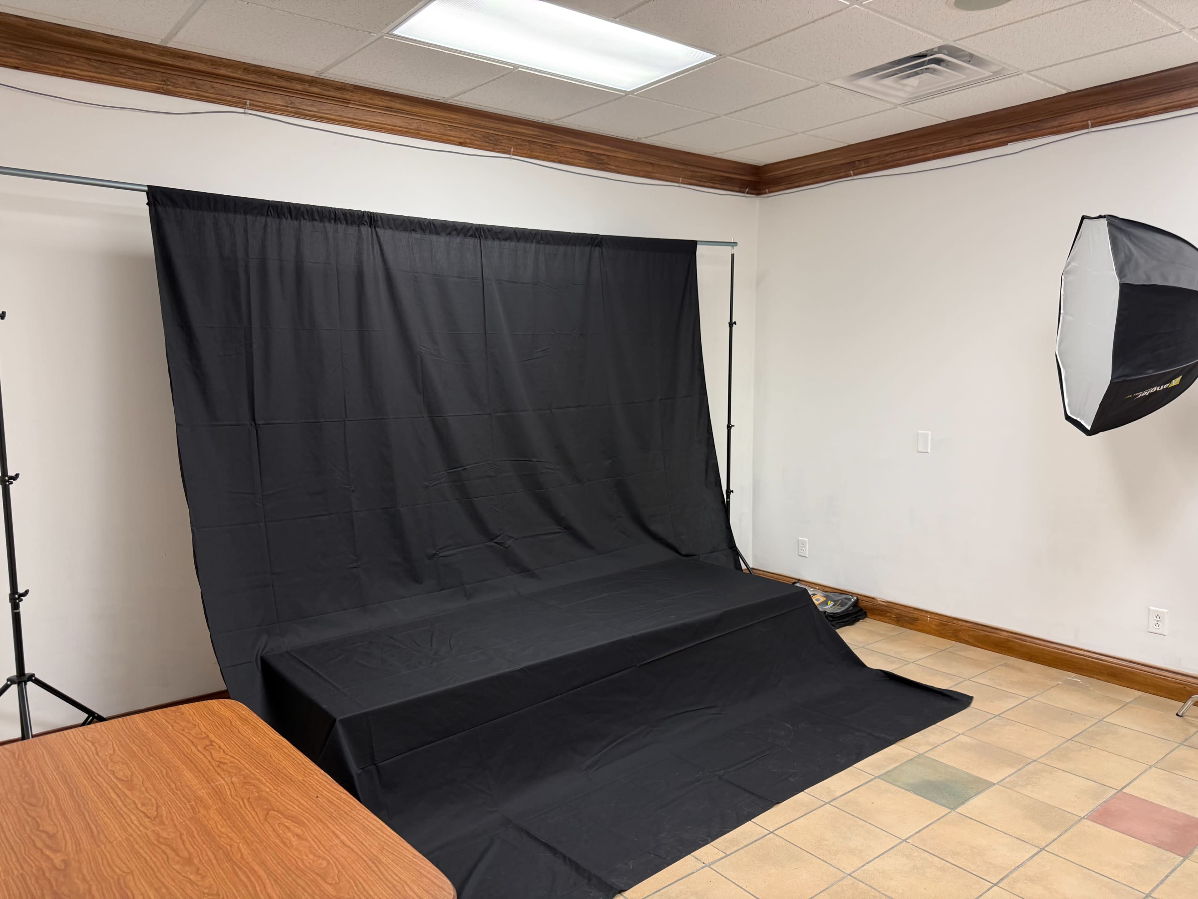 The image shows a room with a black backdrop and lighting setup, intended for photography, alongside a table in the foreground.