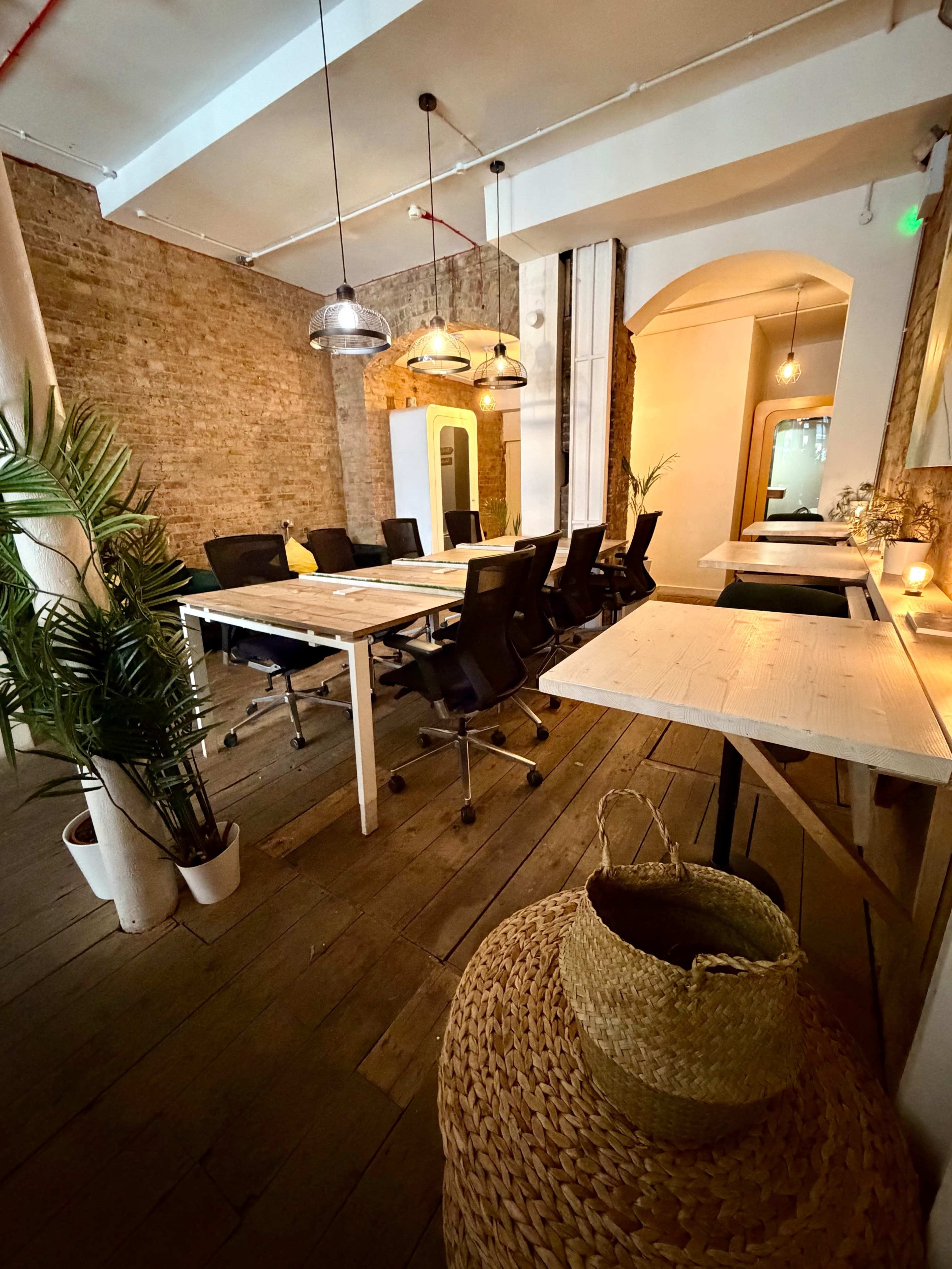 A modern conference room features a long white table surrounded by black chairs, with exposed brick walls and green plants in the decor.