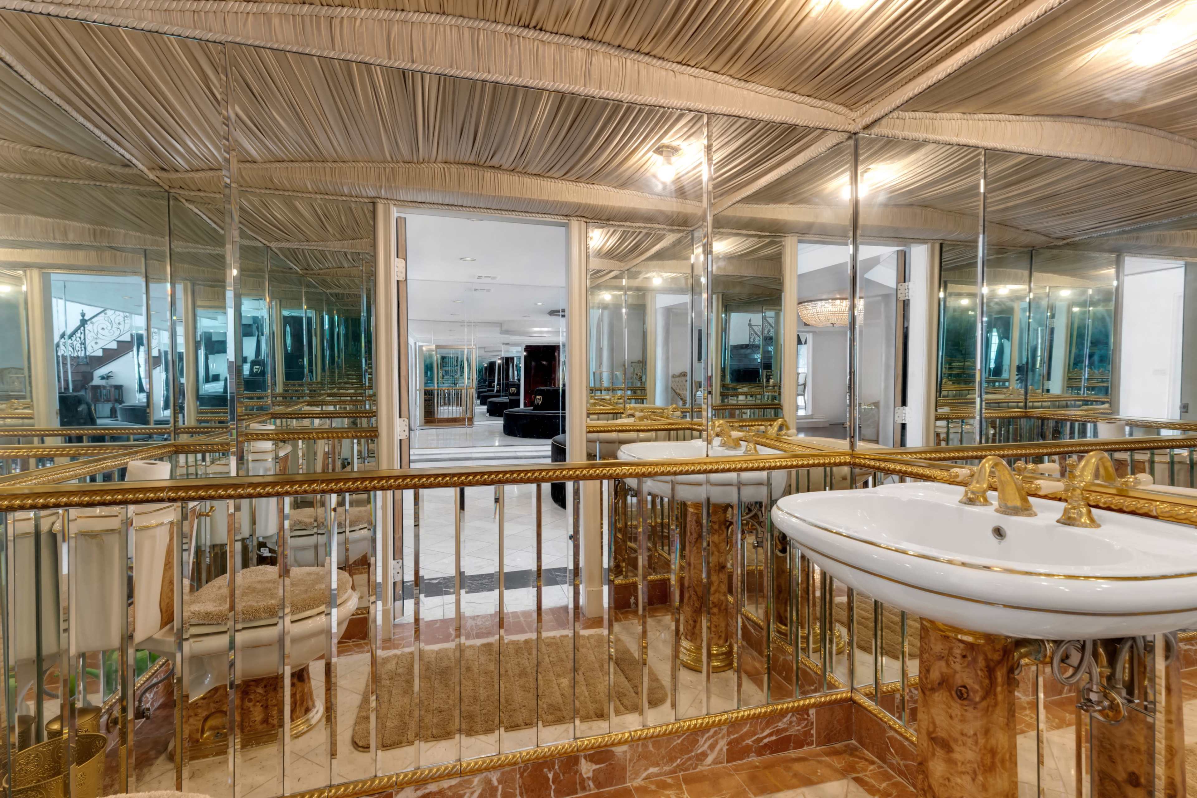 The image shows a luxurious bathroom featuring a gold-accented sink, extensive mirrors, and plush carpeting.