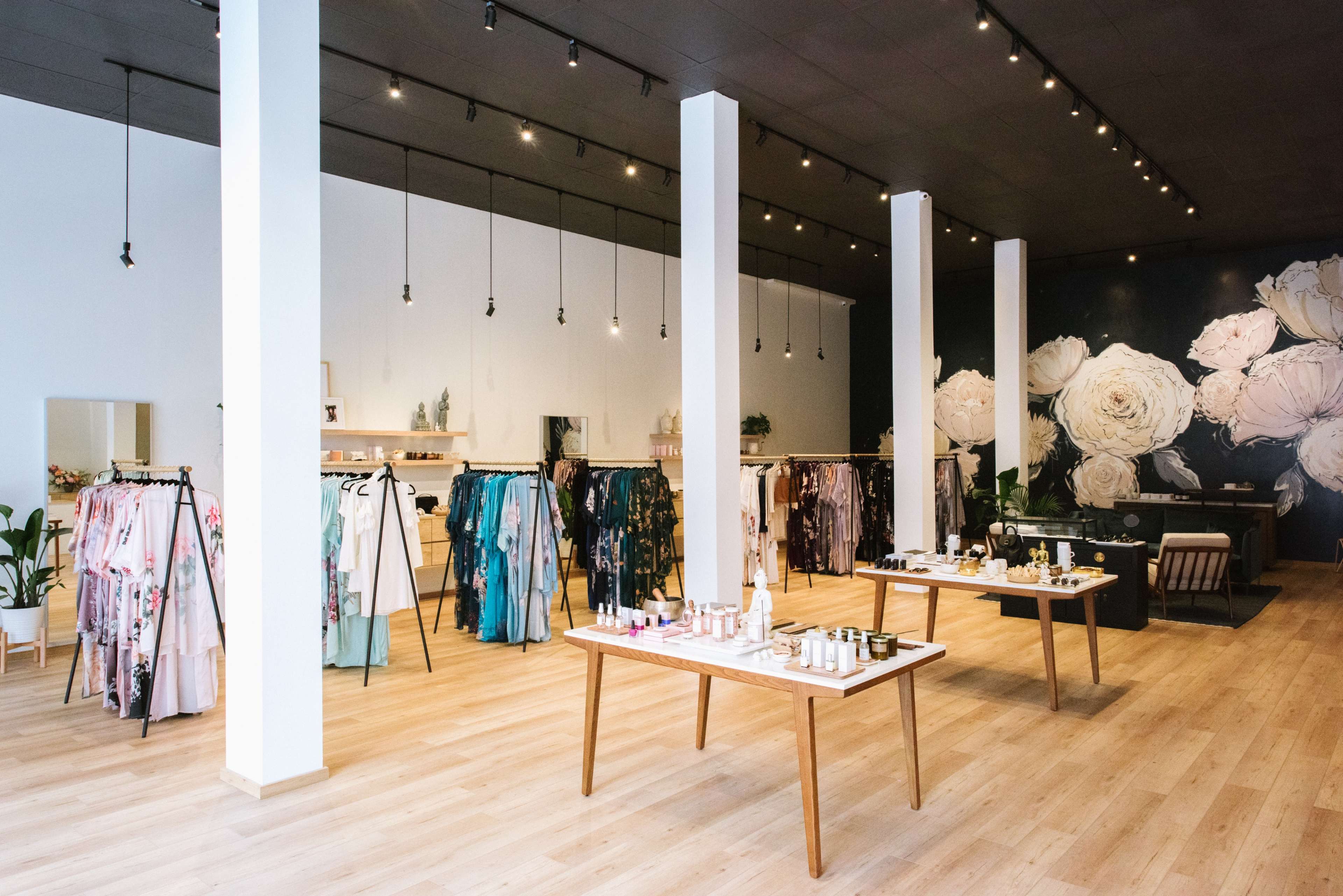 A boutique with clothing racks displaying colorful garments and tables featuring various beauty products in a well-lit space.