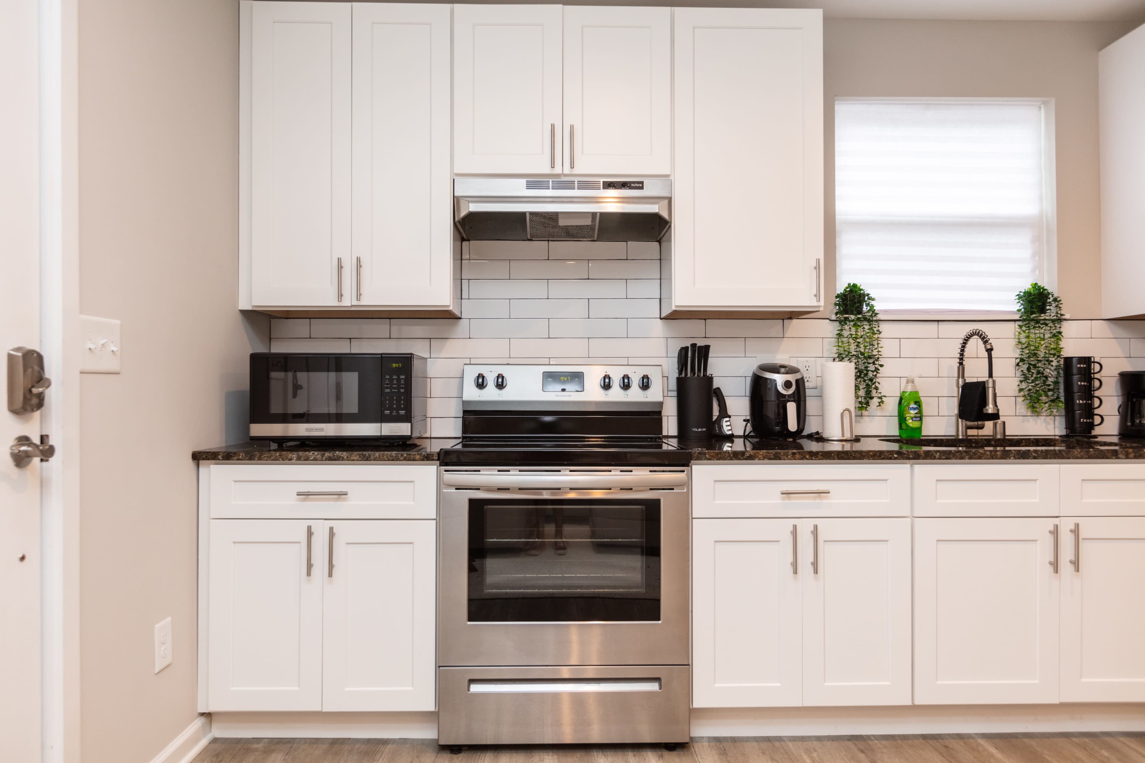 A modern kitchen features stainless steel appliances, including an oven, microwave, and coffee maker, against white cabinetry and a tiled backsplash.