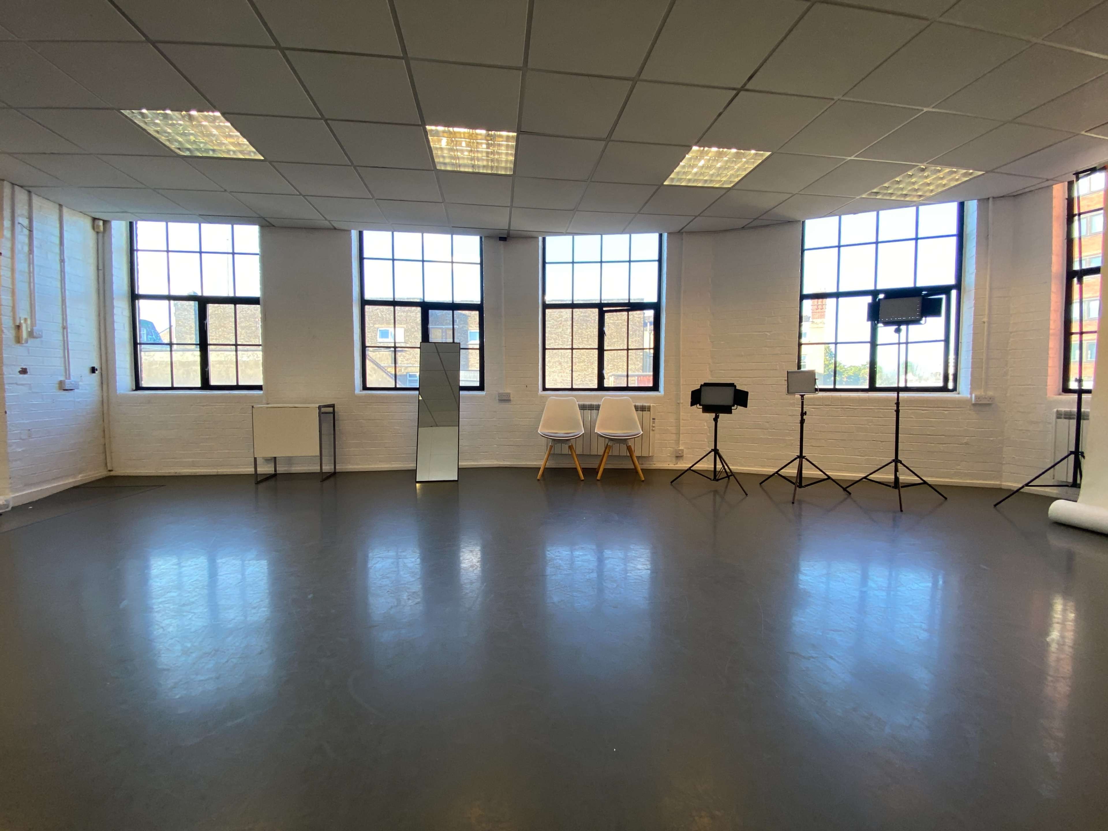 A bright room with large windows, two chairs, a mirror, and several stands for lighting or cameras.