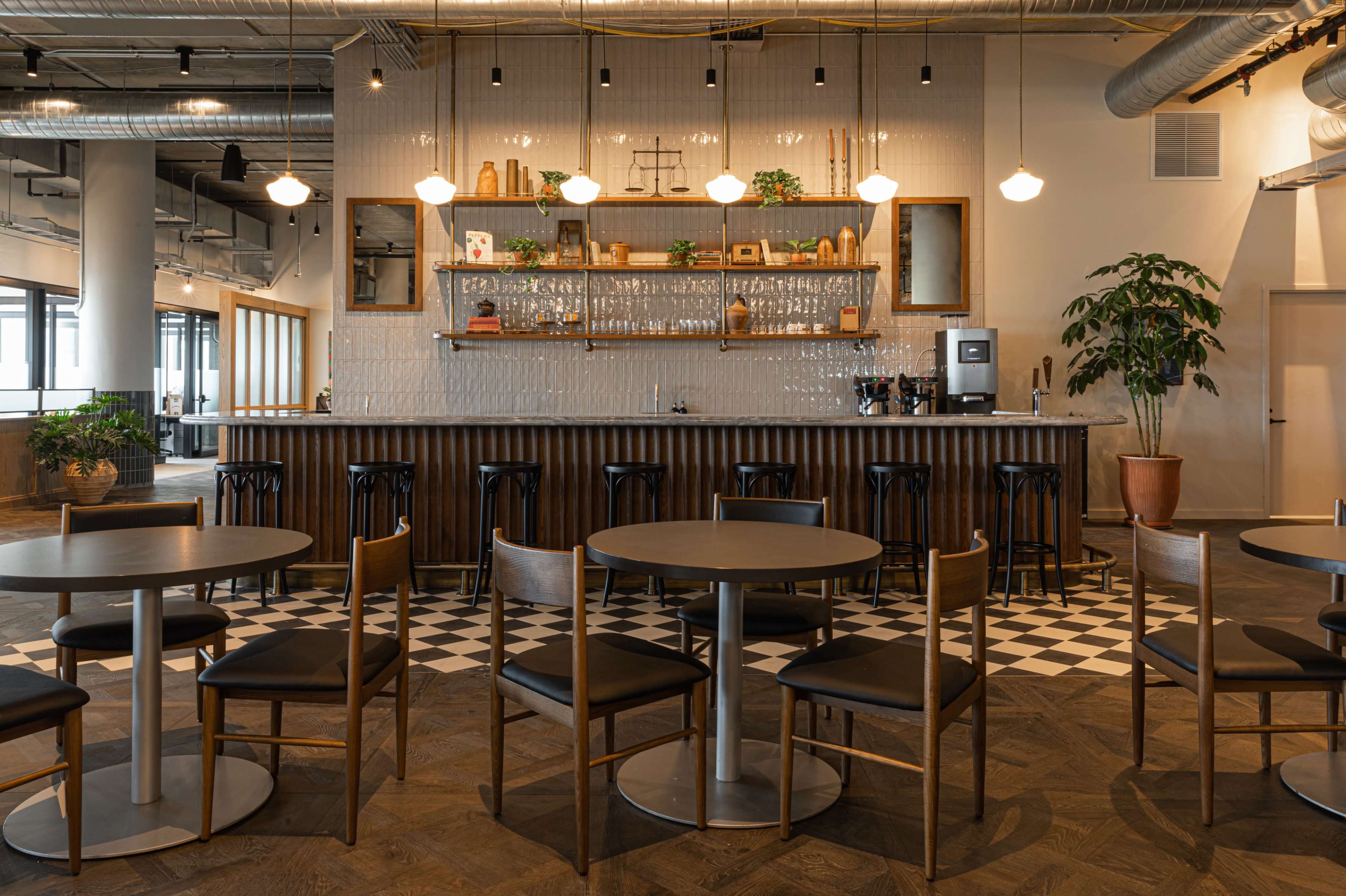 A modern café interior with a bar area featuring a counter, shelves, and round tables arranged with chairs against a checkered floor.