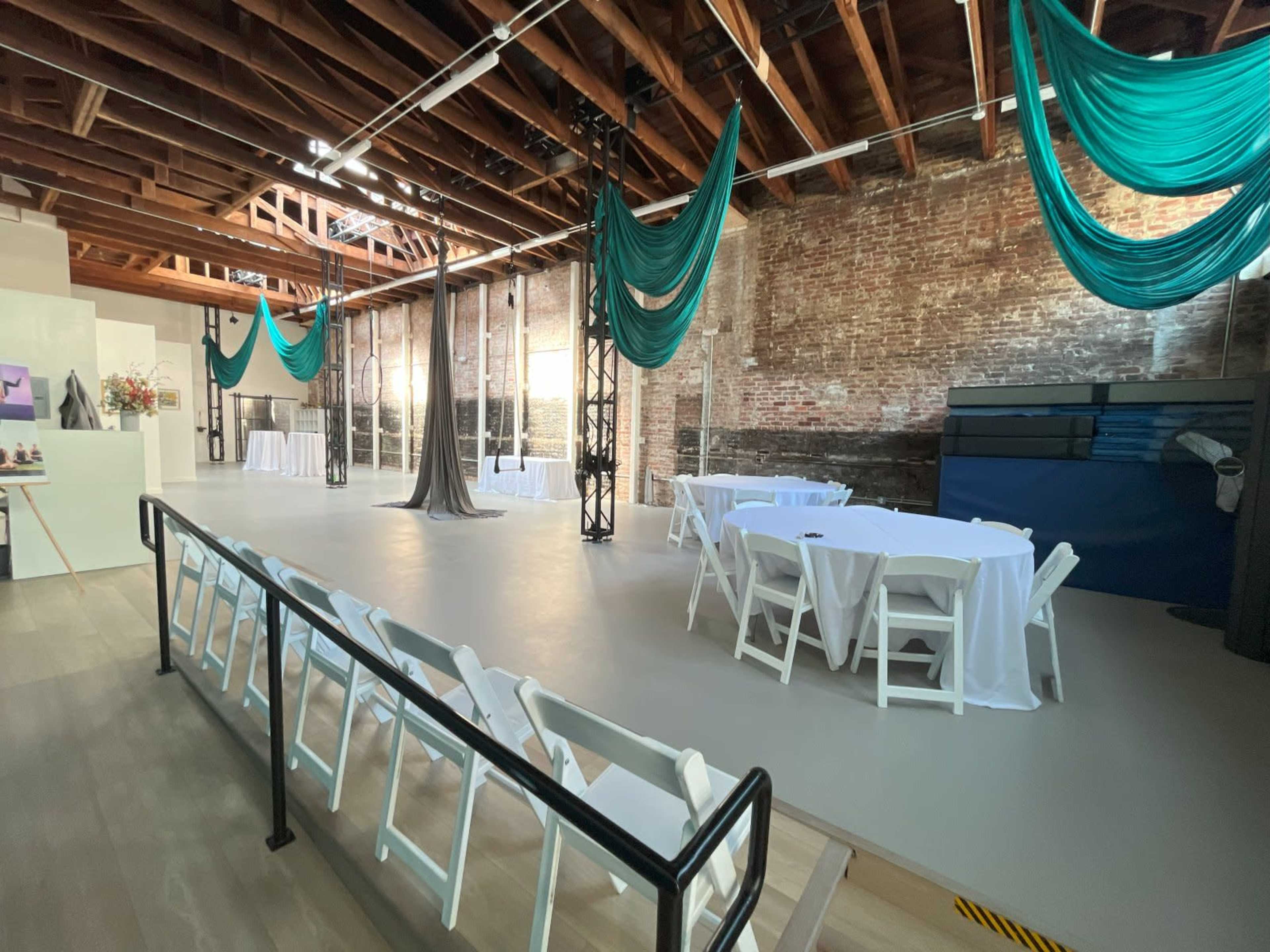 A spacious venue with exposed brick walls, white tables set with tablecloths, and teal fabric draped from the ceiling.