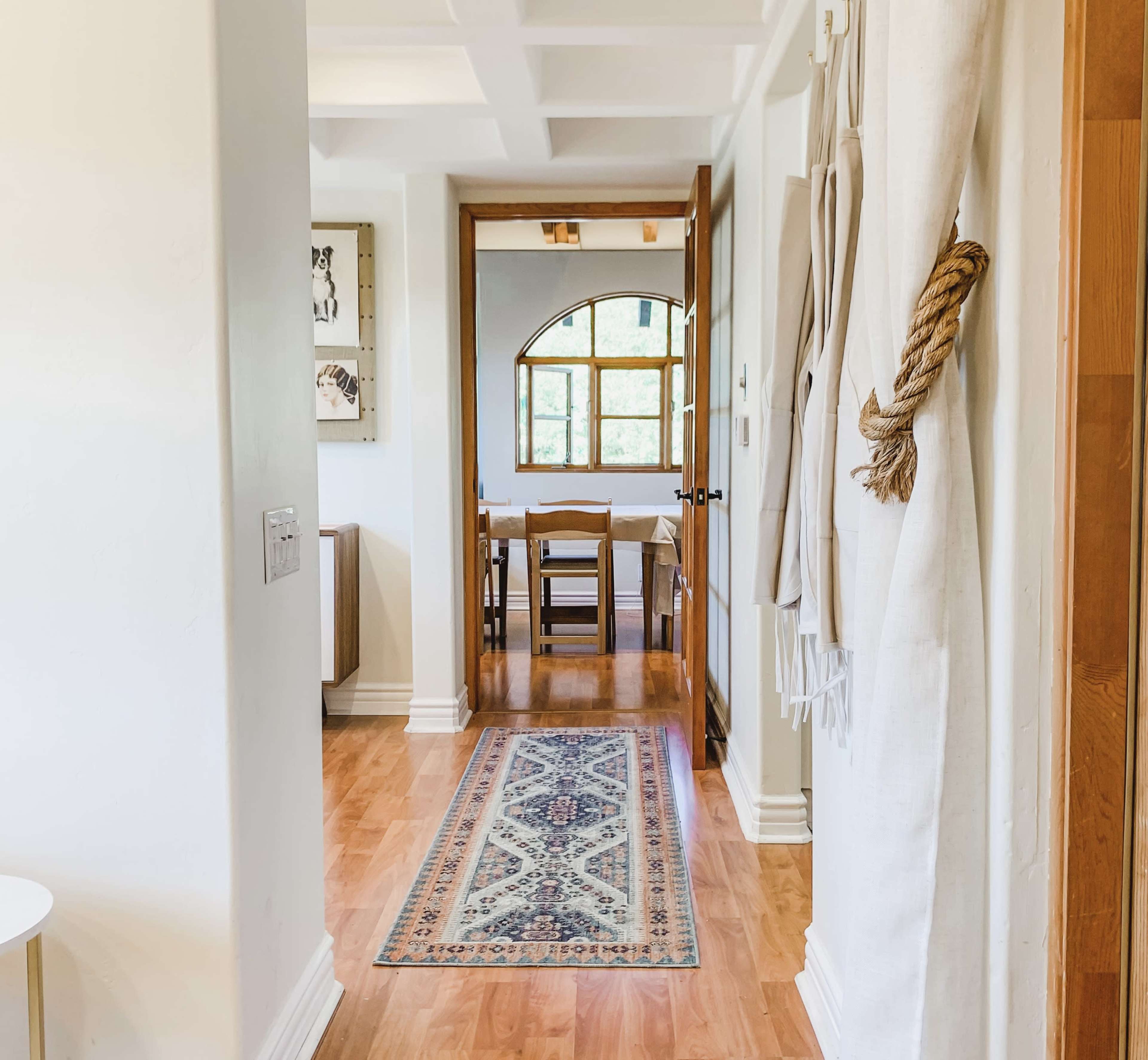 A hallway leading to a dining area, with a patterned rug on the wooden floor and an arched window at the back.