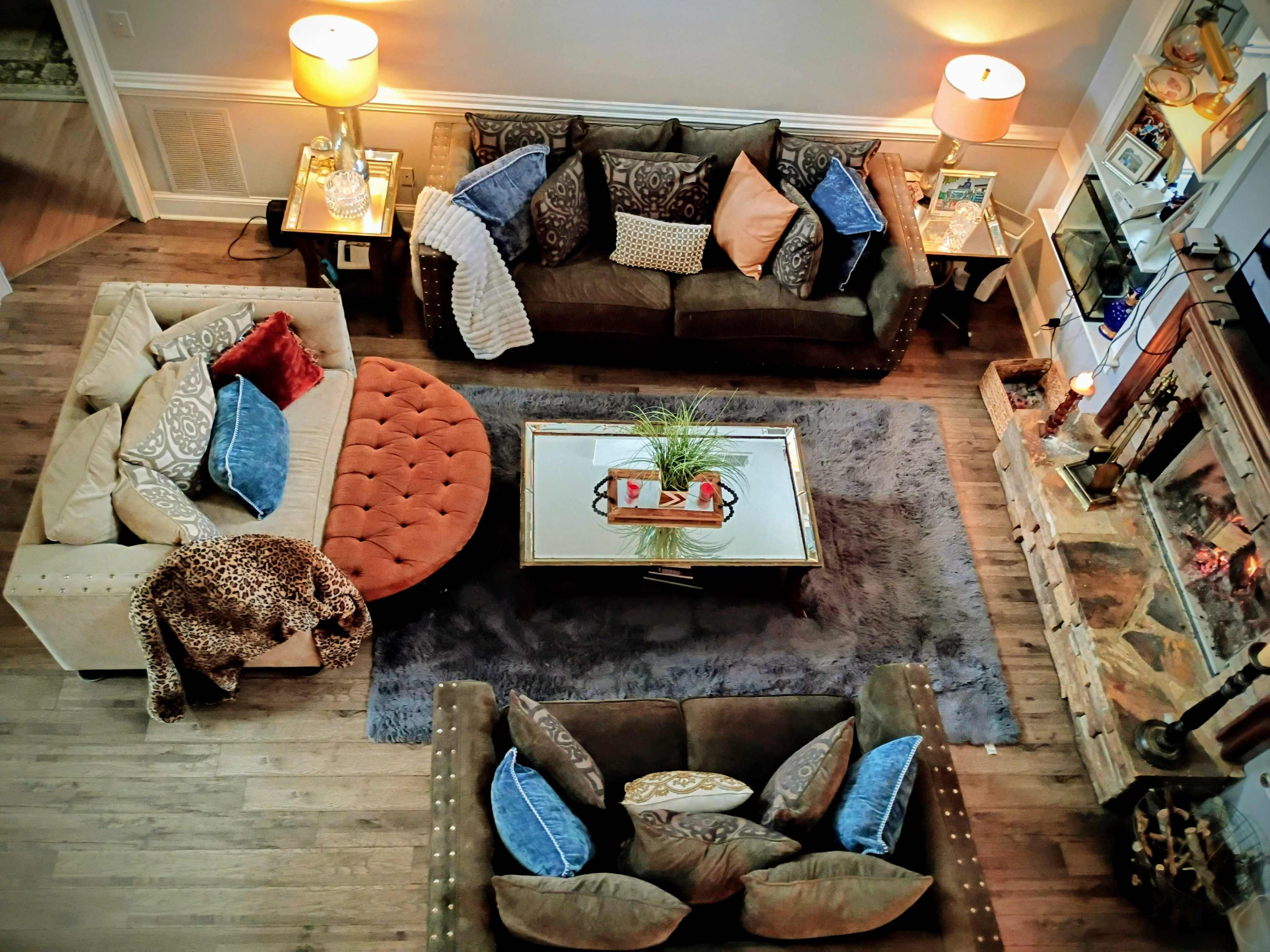 The image shows a living room with two sofas, a round ottoman, a coffee table, and a fireplace, all arranged on a large area rug.