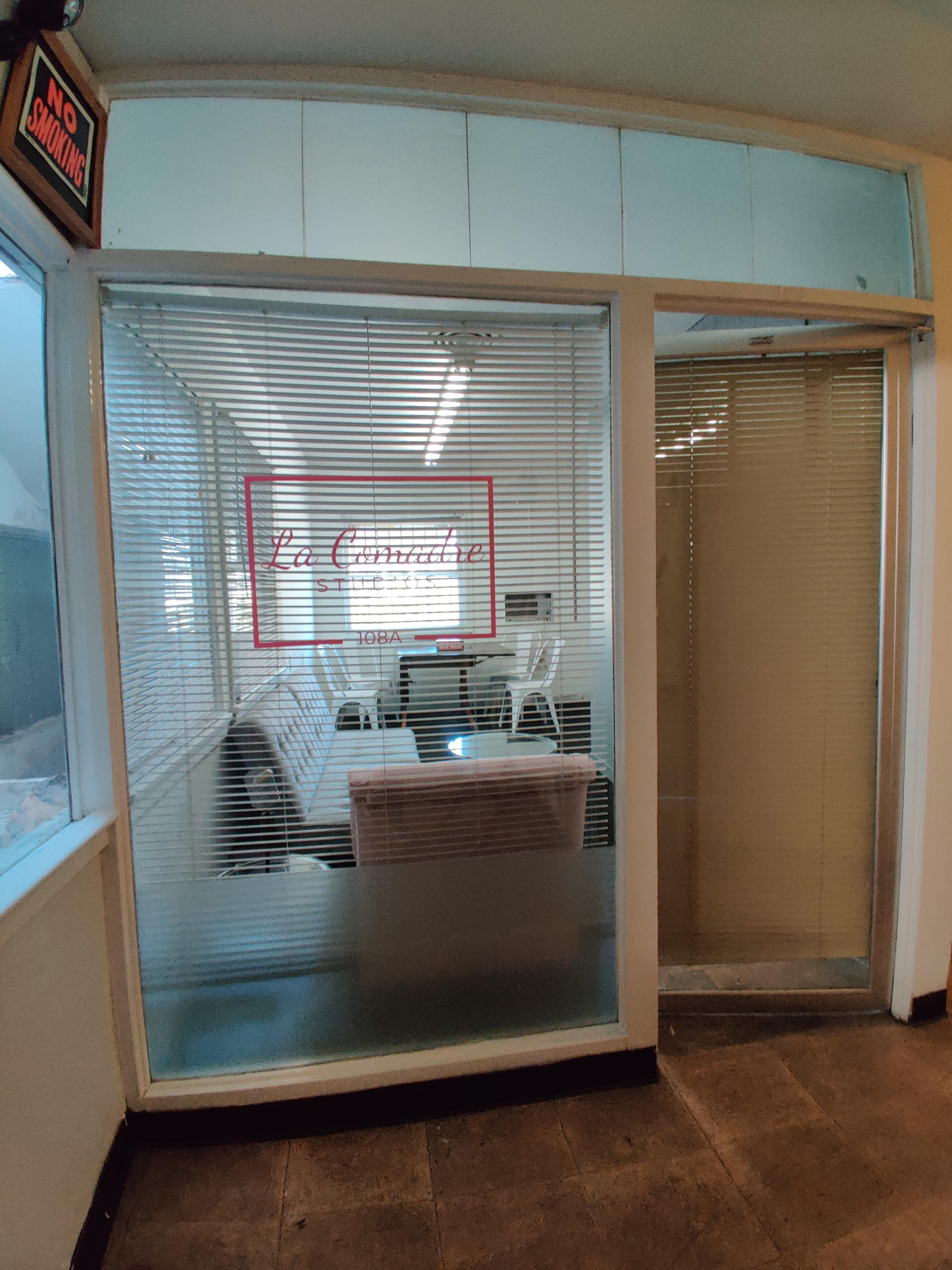 A glass door with blinds, leading to a waiting area labeled "La Consultora" with chairs and a couch visible inside.