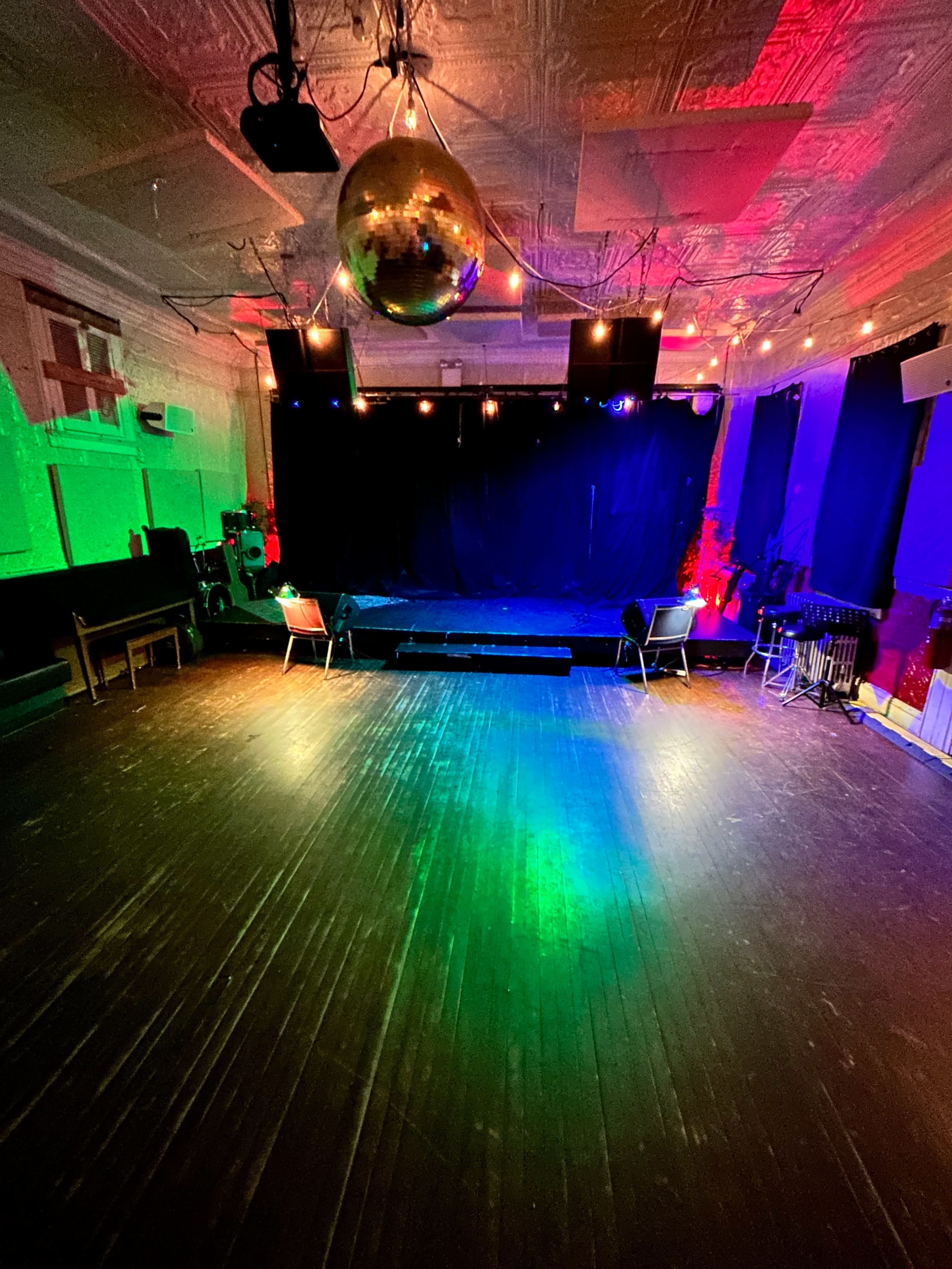 The image shows an empty performance space with a disco ball overhead and colorful lights illuminating the stage area.