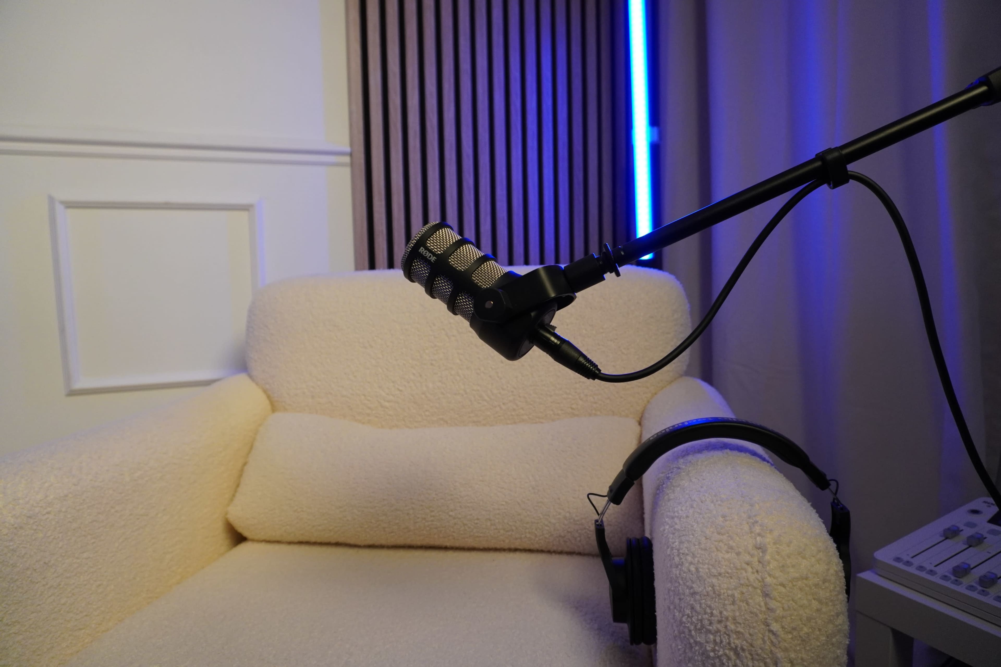 A microphone mounted on a stand is positioned near a cozy, cream-colored armchair with a pair of headphones resting on the armrest.