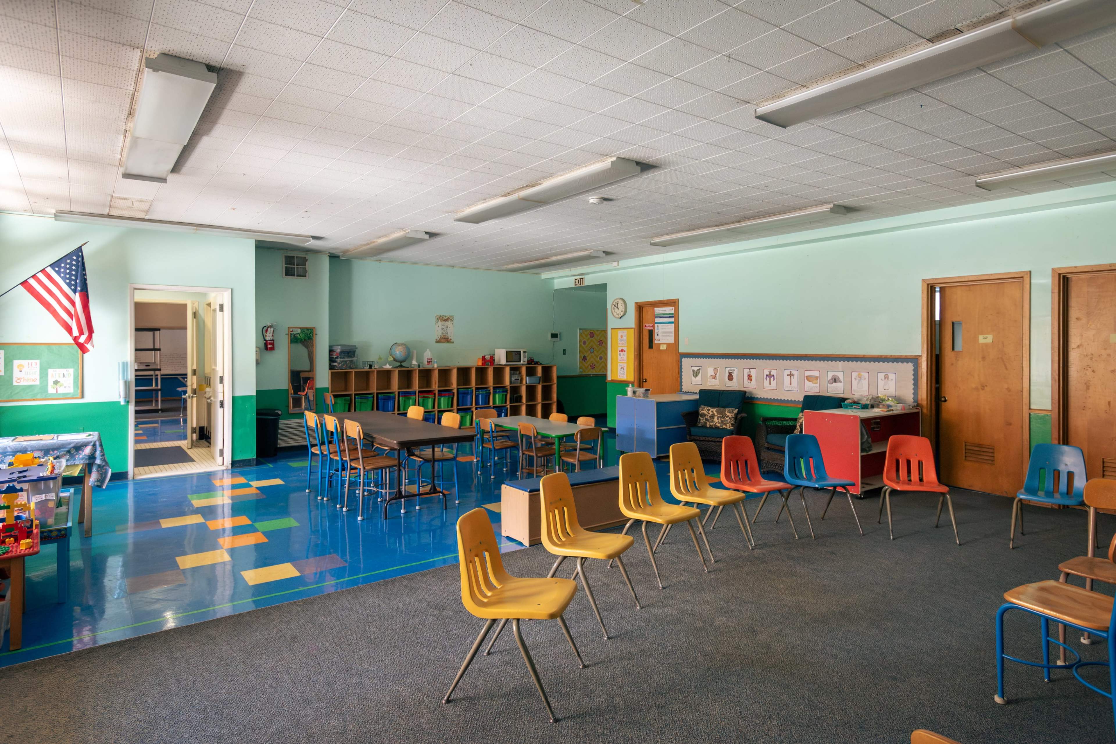 A brightly colored classroom features multiple chairs arranged in a circle with a table and shelving units against the walls.