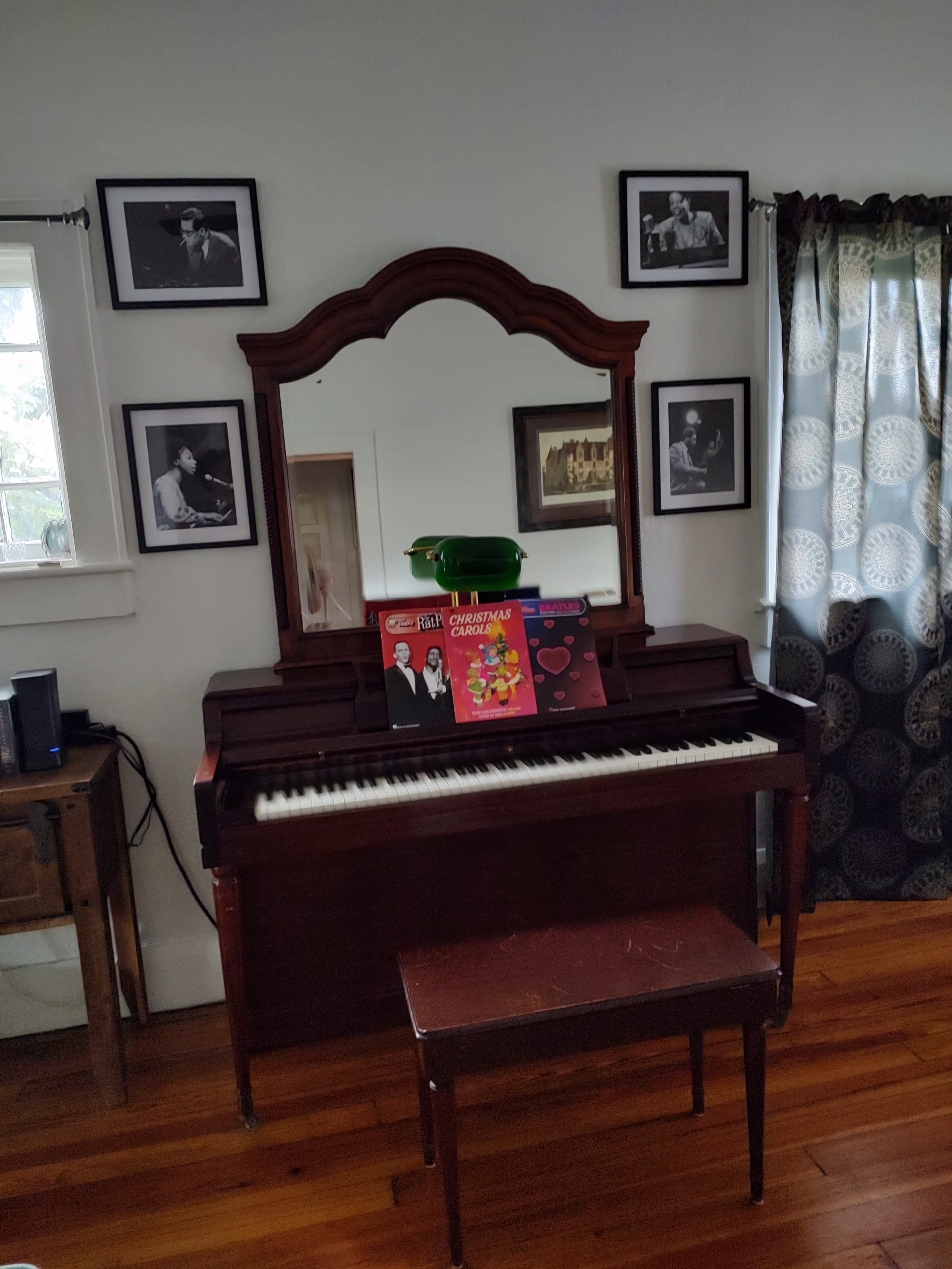 A vintage piano with sheet music and records displayed on top is positioned against a wall adorned with framed black-and-white photographs.