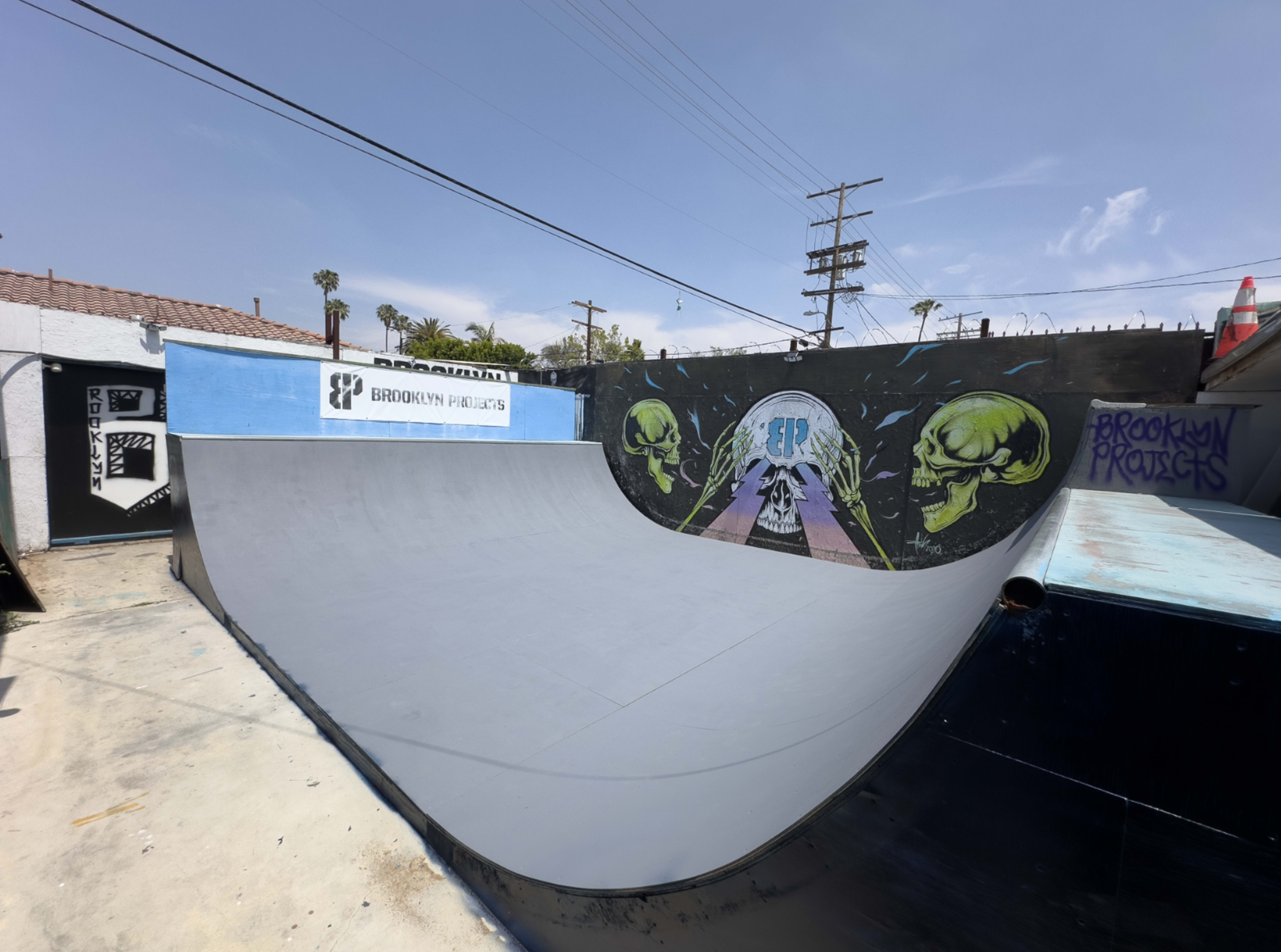 The image shows a skateboarding ramp with a mural featuring skulls and graffiti on the surrounding walls.