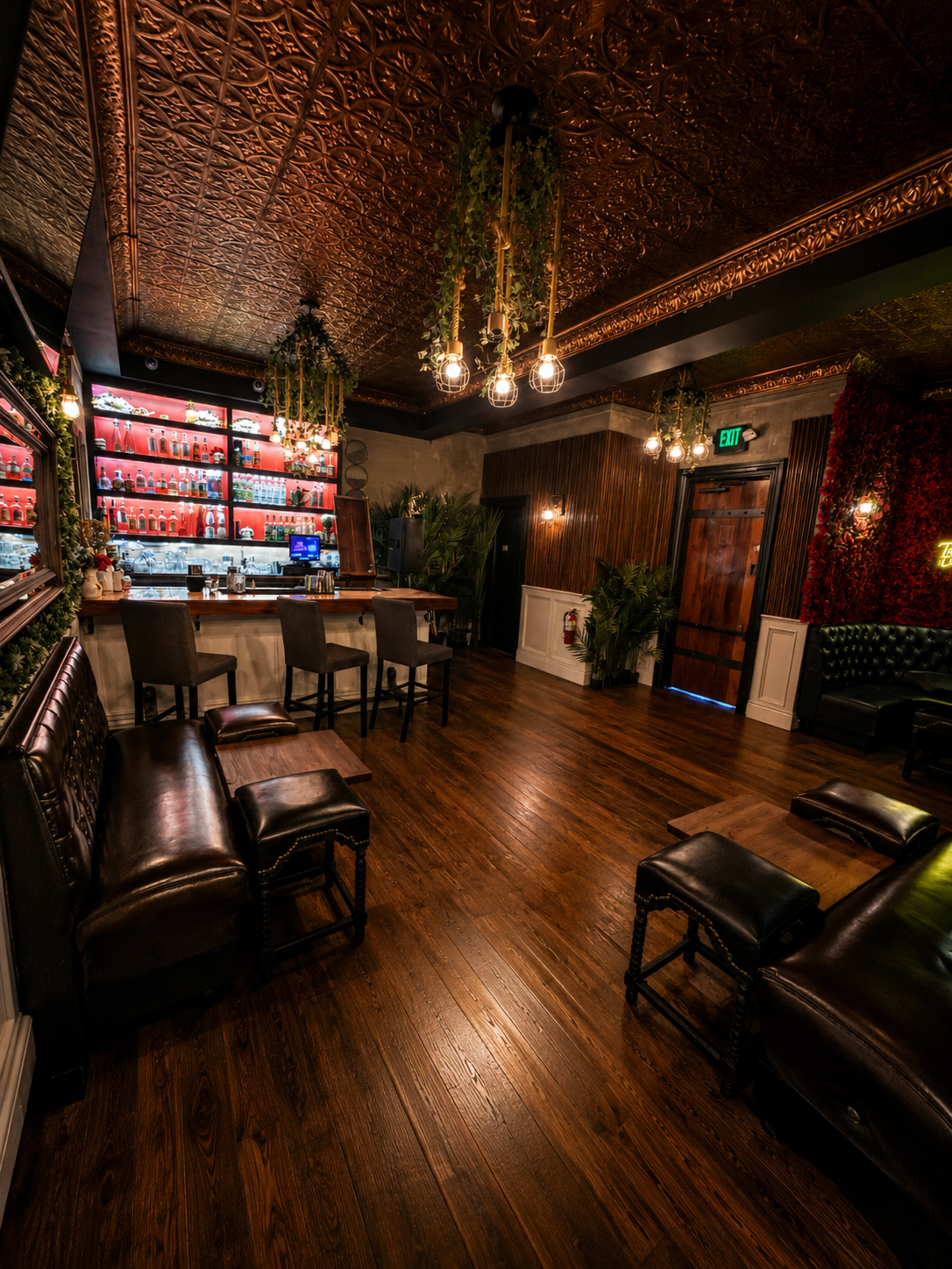 The image shows a dimly lit bar interior with wooden flooring, ornate ceiling details, a well-stocked back bar, and various seating arrangements.