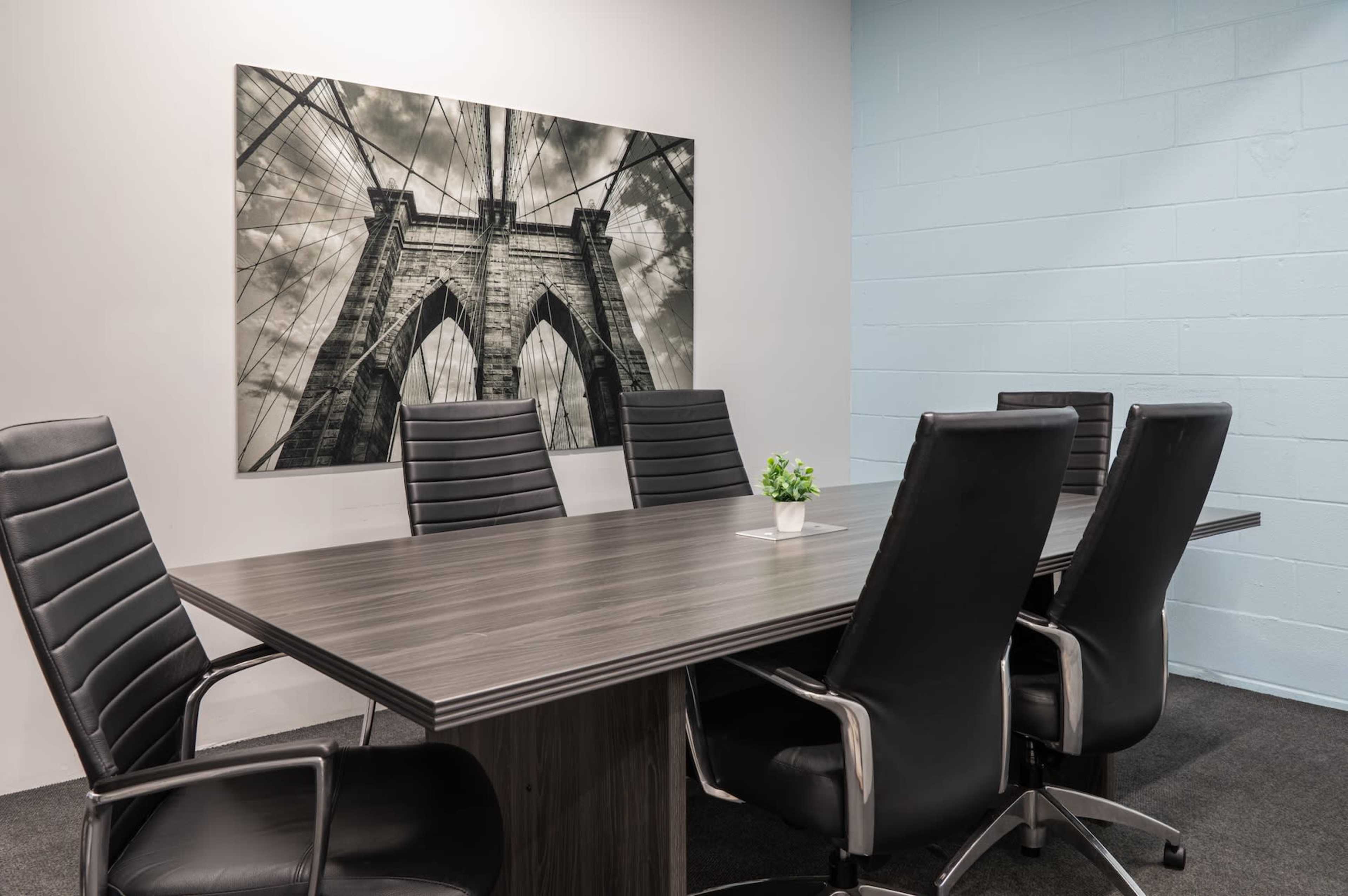 A conference room features a large table surrounded by black leather chairs and a black-and-white photograph of a bridge on the wall.
