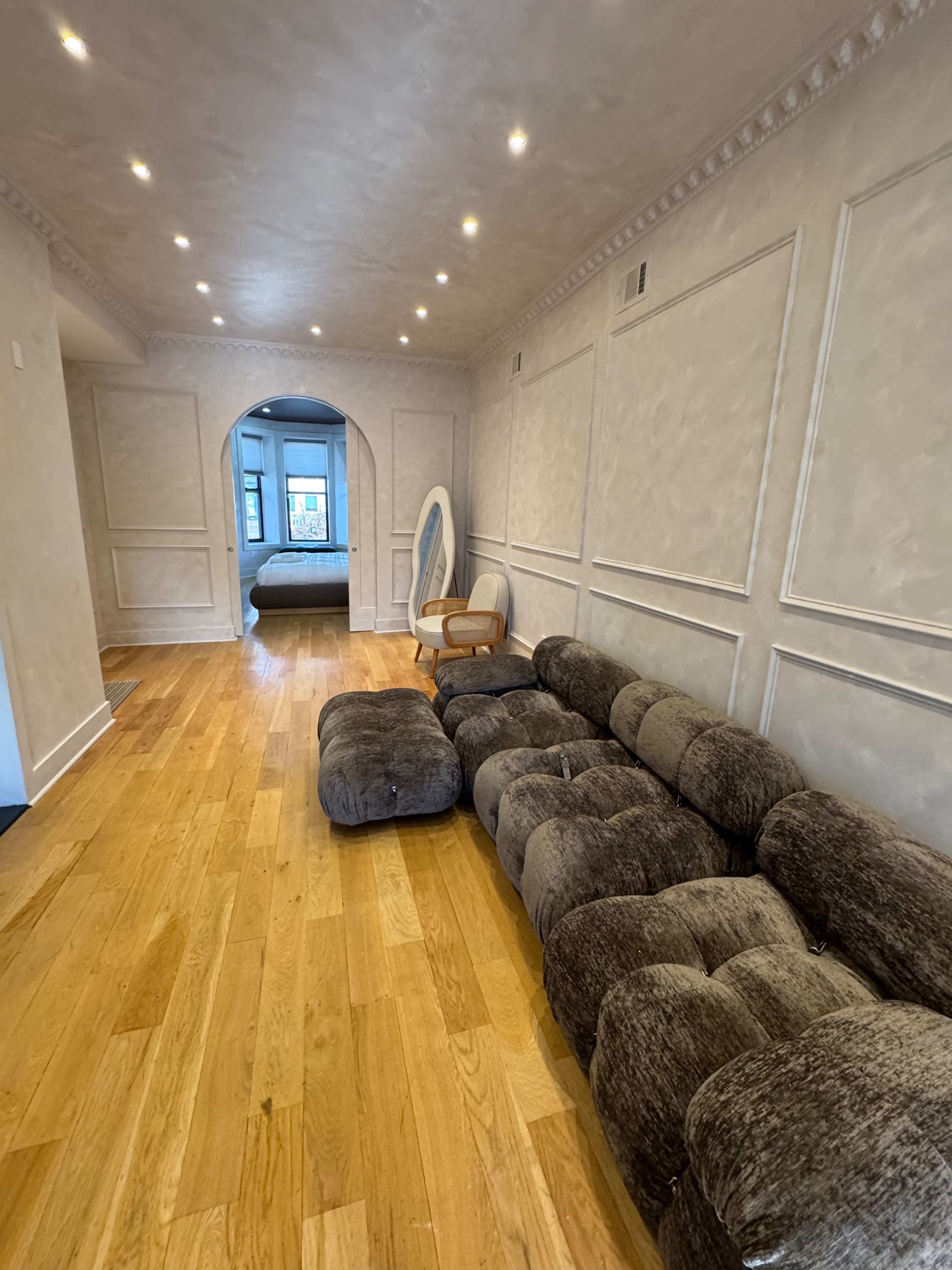A long hallway features a plush brown sectional sofa and an arched doorway leading to a bedroom.