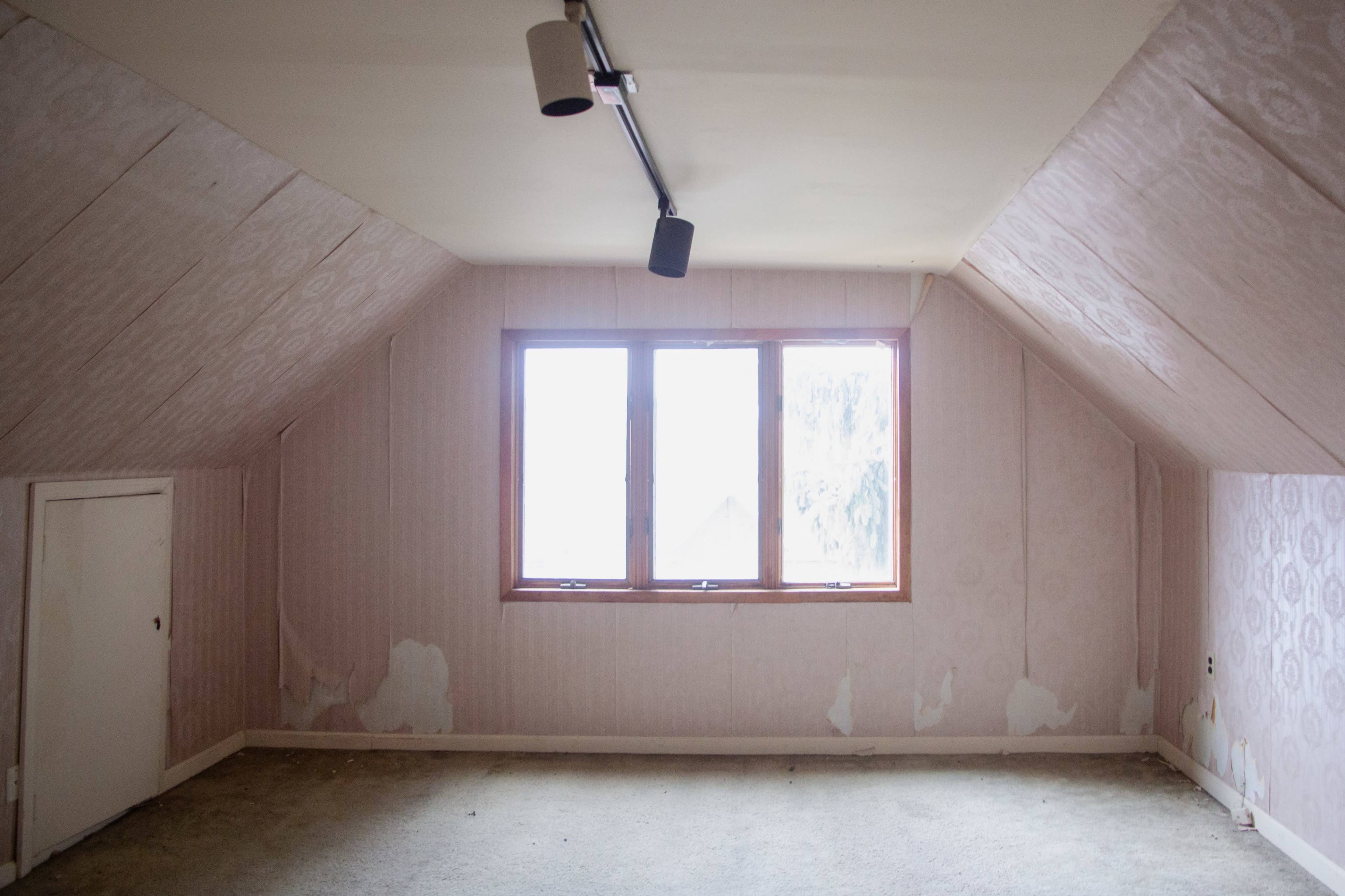 The image shows a sparsely furnished attic room with peeling wallpaper, a window, and a bare floor.