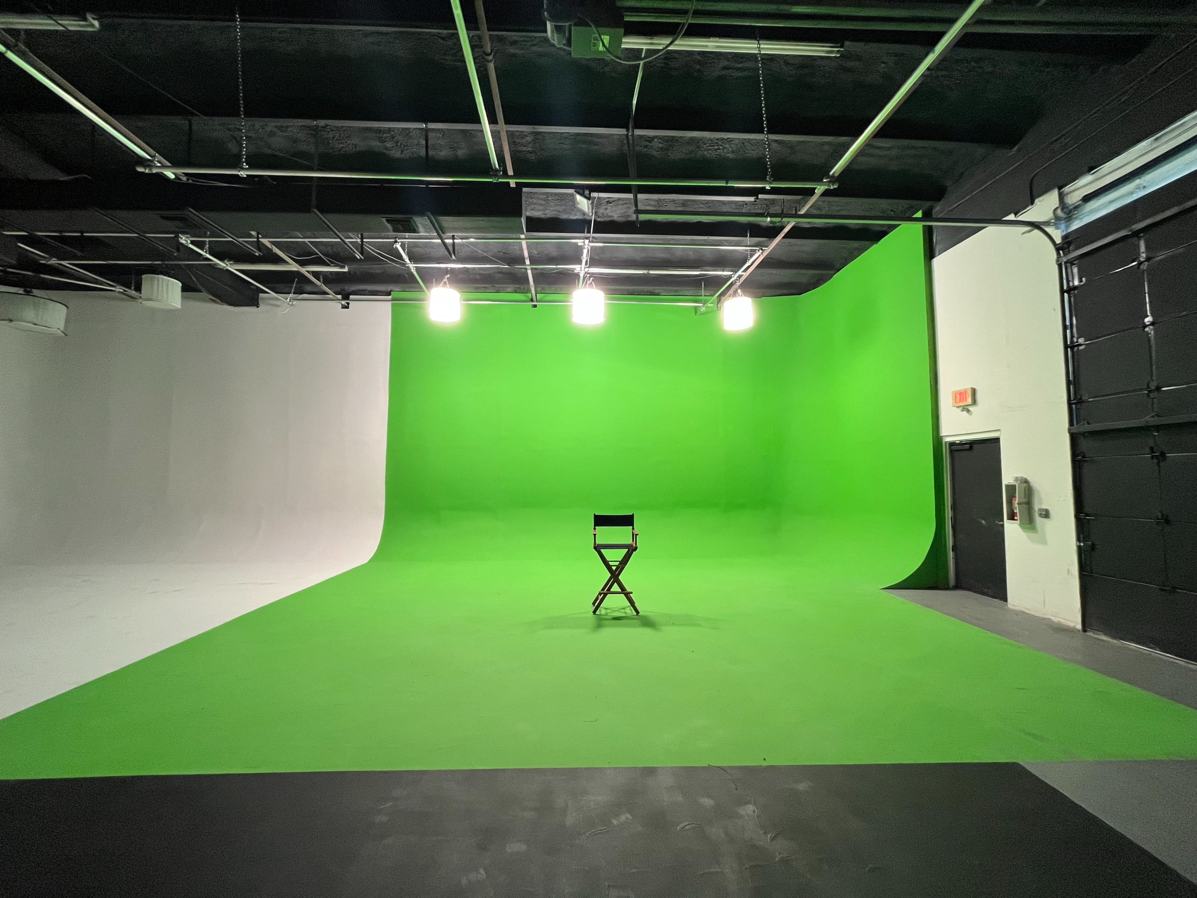 A large studio space featuring a green backdrop, a director's chair in the center, and overhead lighting fixtures.