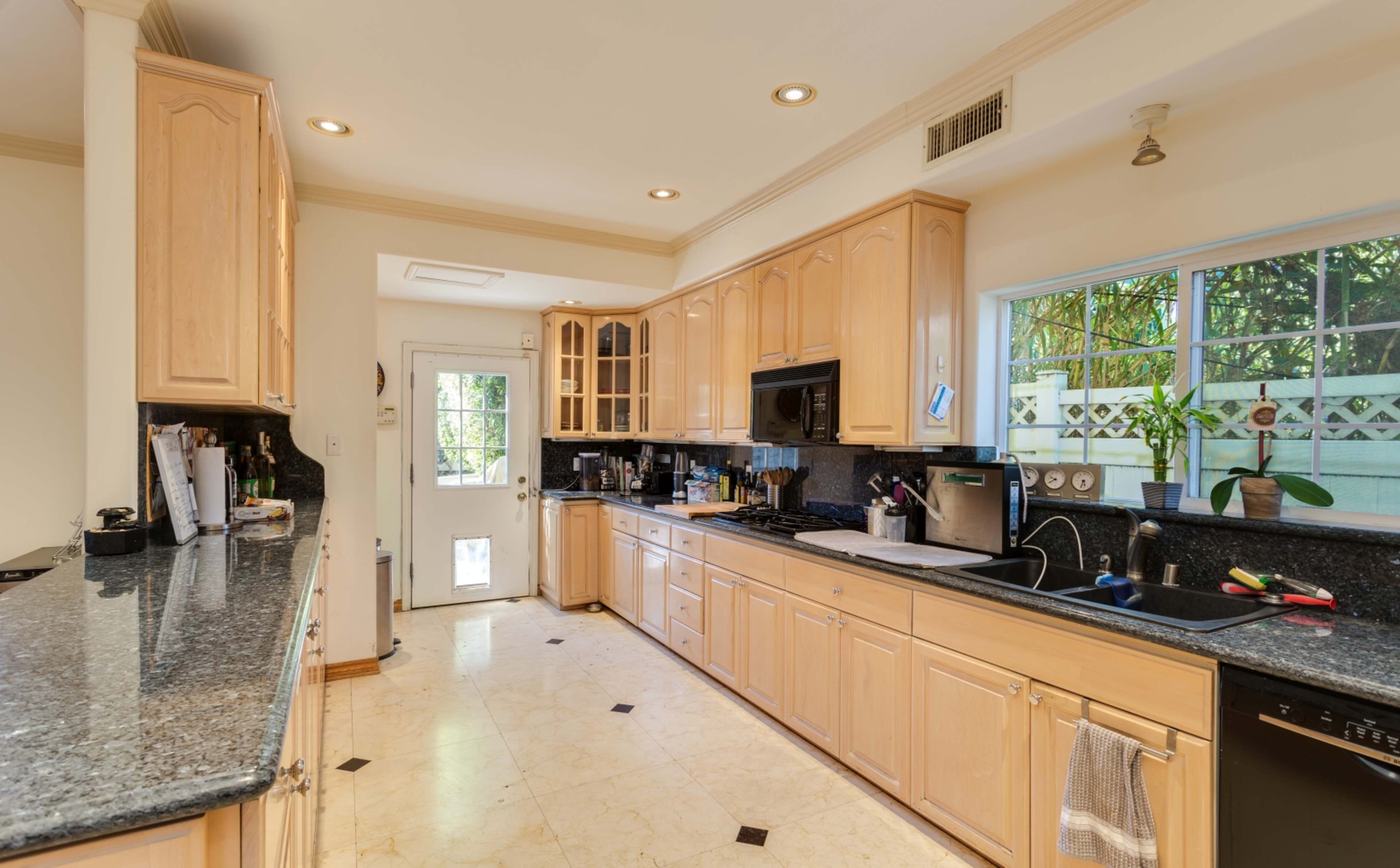 A kitchen with wooden cabinetry, a black granite countertop, and a window above the sink.