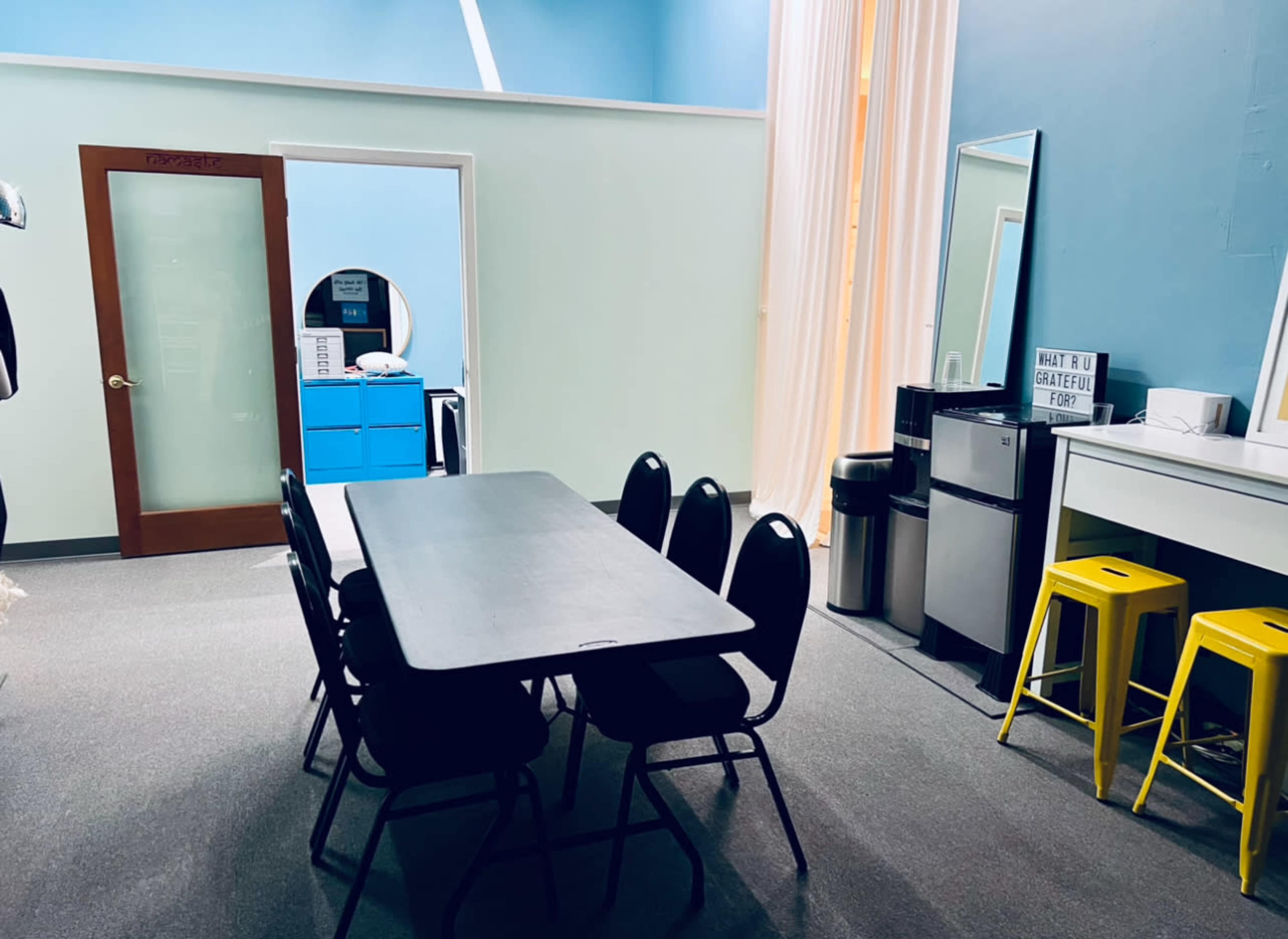 A conference room with a large table surrounded by six black chairs, a blue cabinet, and a mirror on the wall.