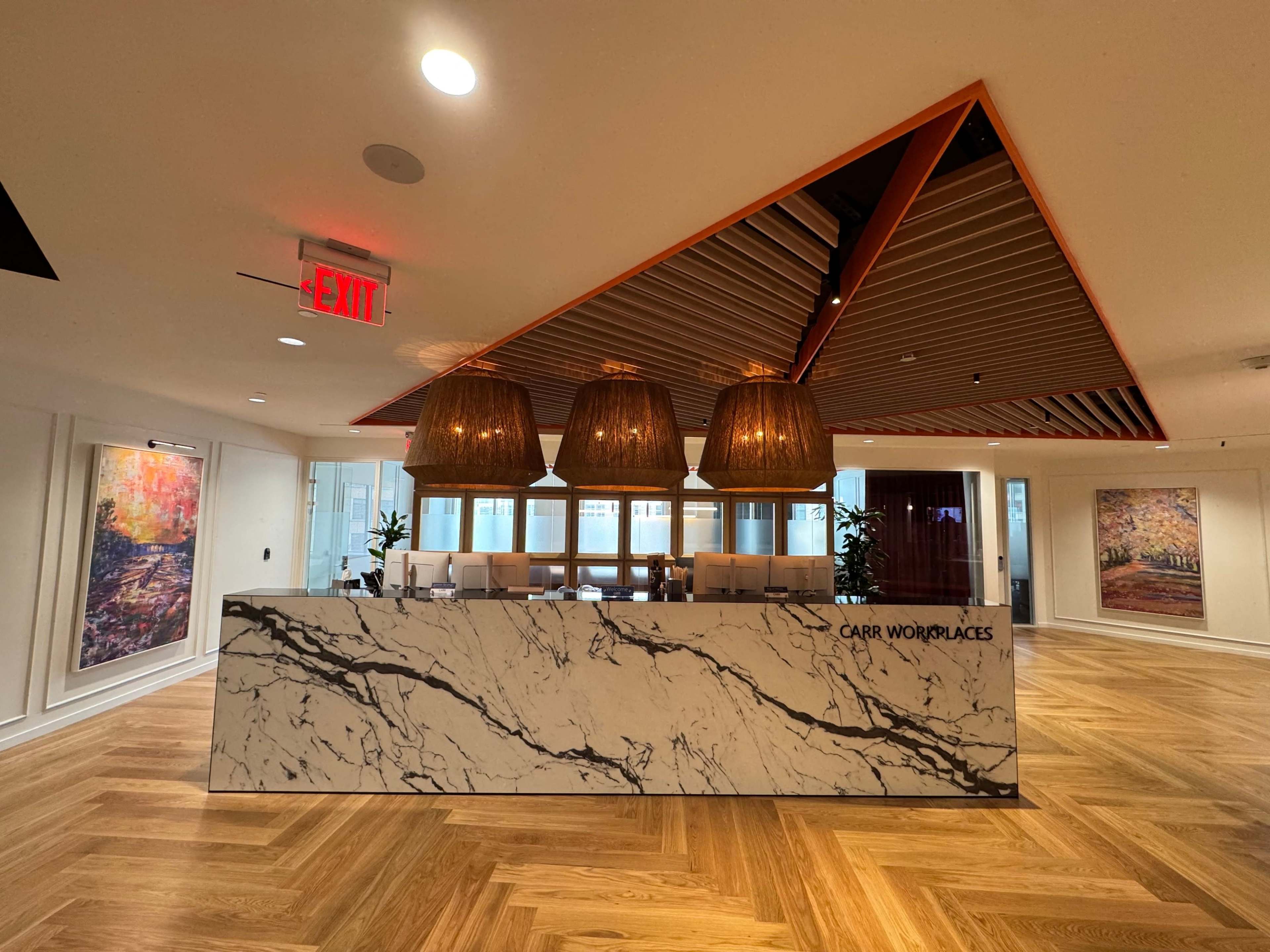 The image shows a modern reception area with a marbled front desk, three large pendant lights hanging above, and large artworks on the walls.