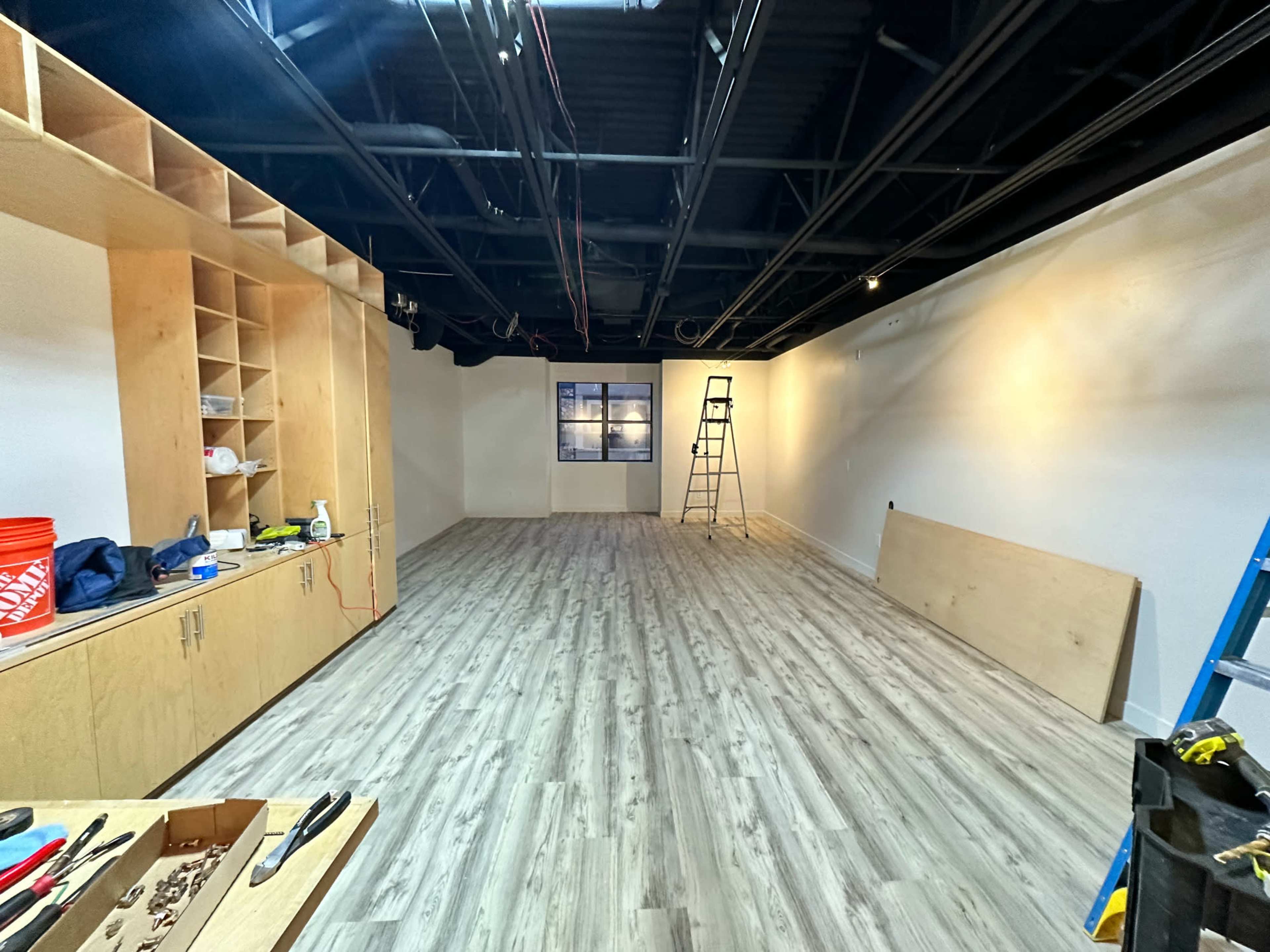An unfinished interior room with light-colored walls, new wooden flooring, and construction materials scattered around.