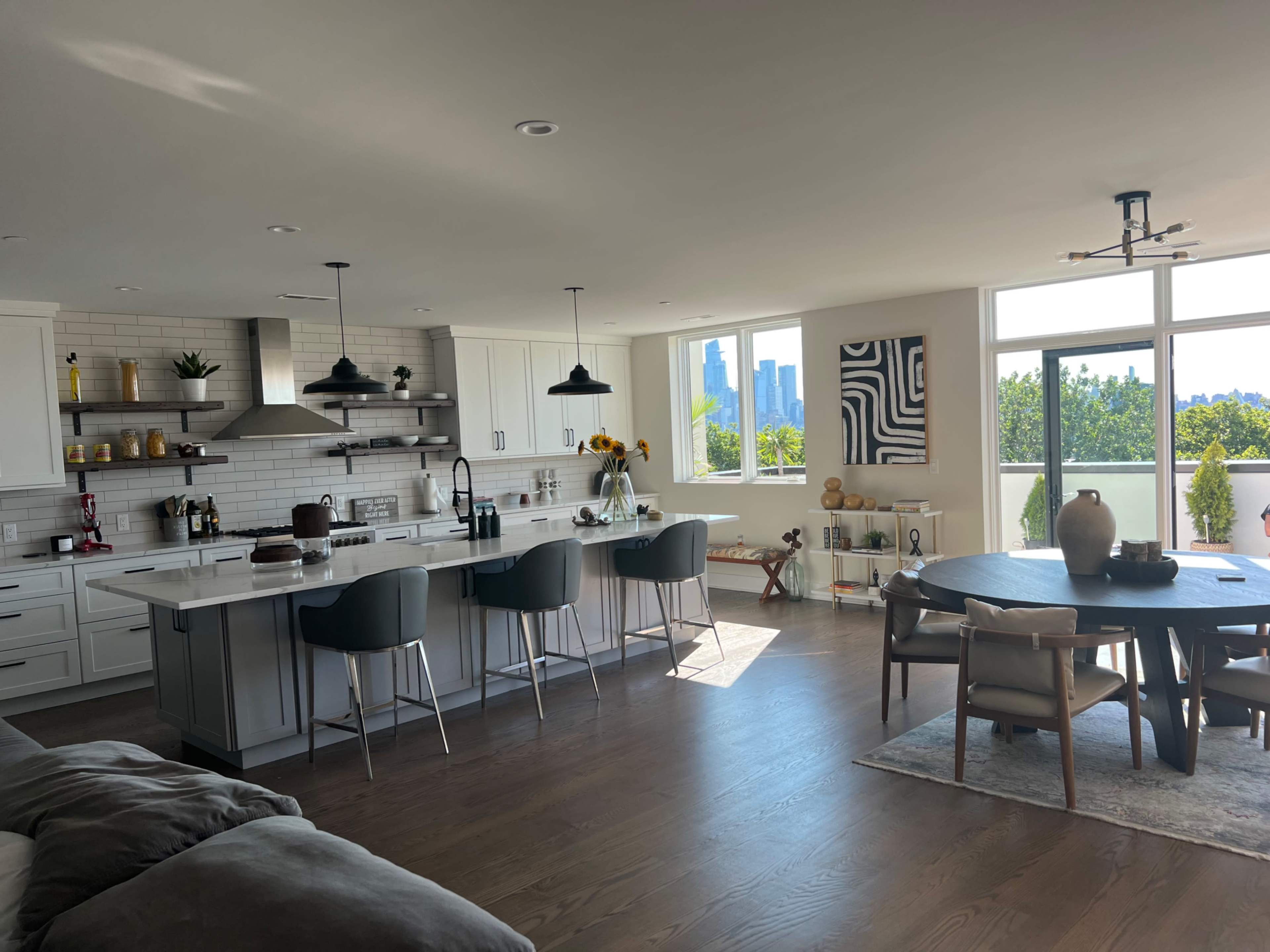 A modern kitchen and dining area with a large island, seating for four, and a panoramic view of a city skyline through large windows.