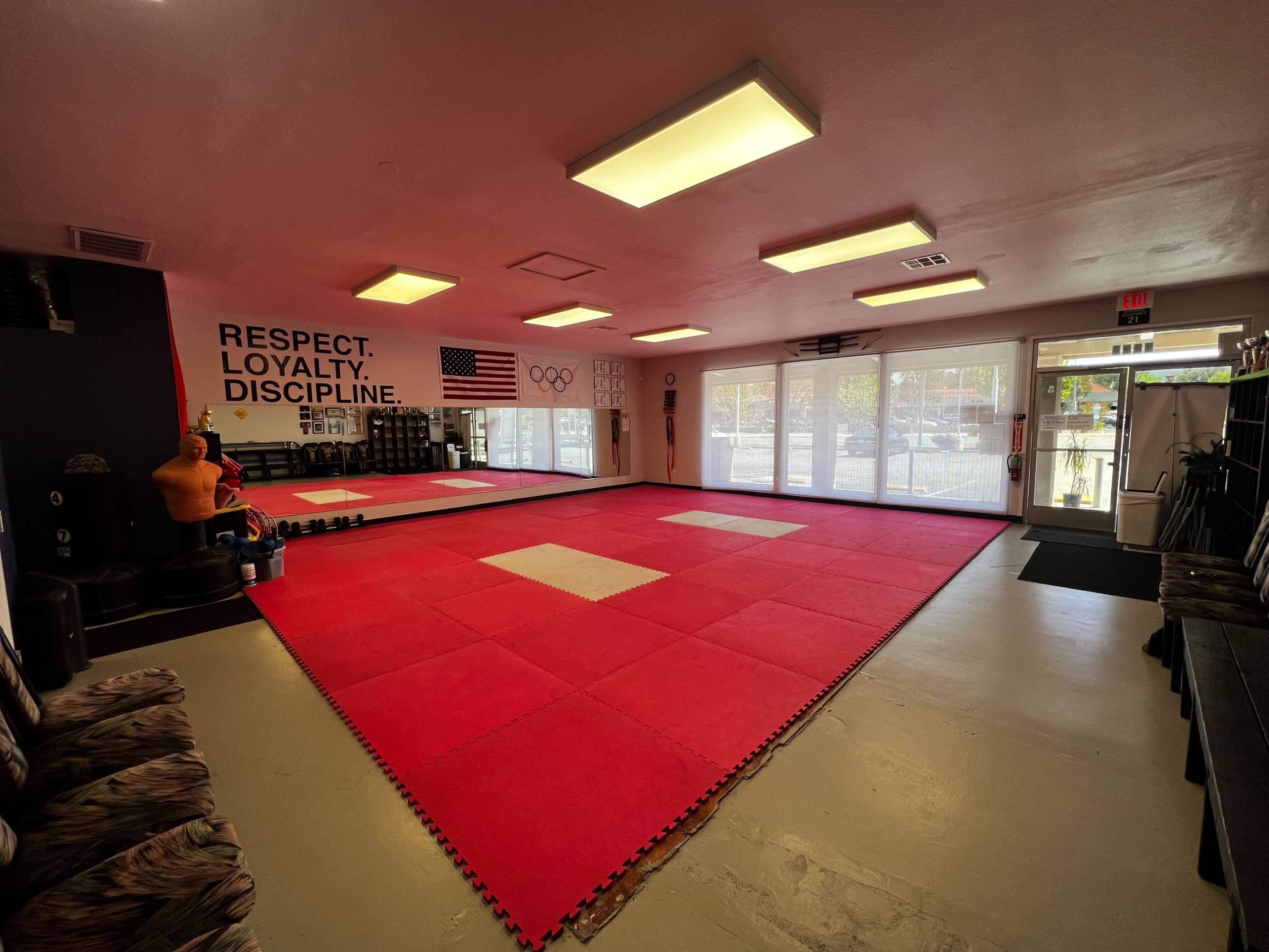 A martial arts studio with a red mat area, walls featuring motivational words, and a view of the entrance doors.