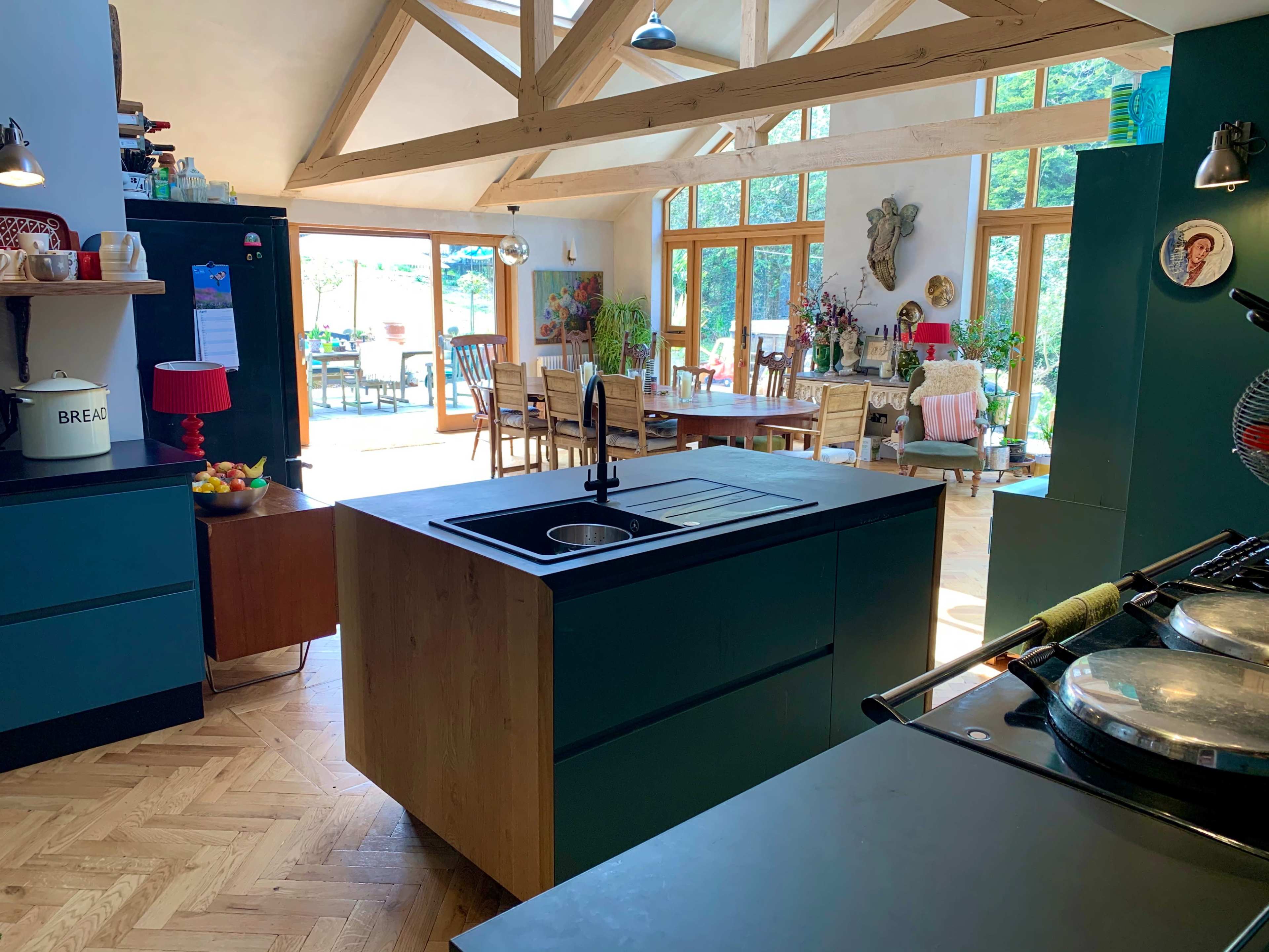 A modern kitchen with an island, featuring wooden beams and large windows that open to a dining area.