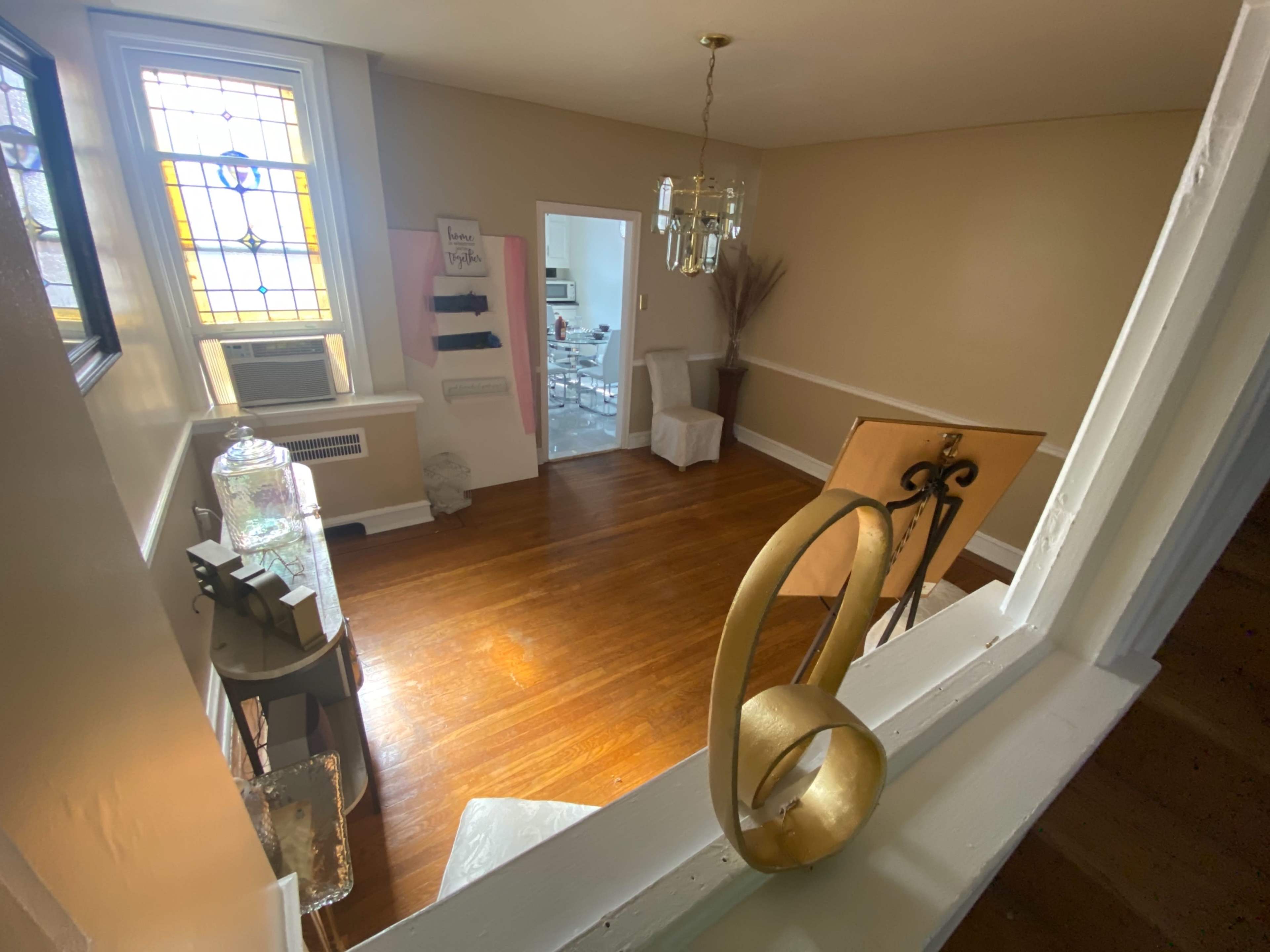 The image shows a well-lit living room with wooden flooring and a decorative chandelier, viewed from an upper perspective.