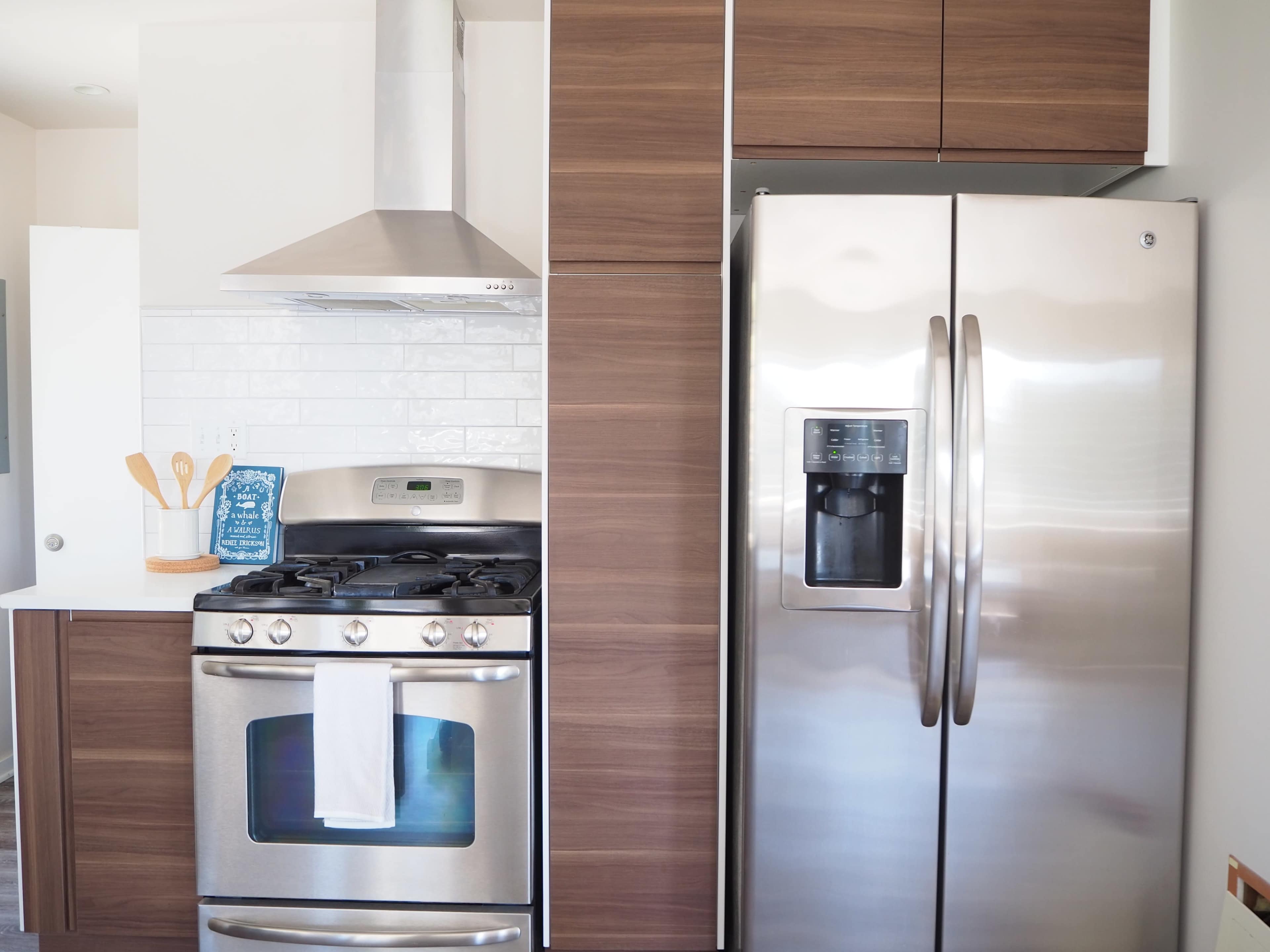 A modern kitchen features a stainless steel refrigerator, a gas stove with an overhead hood, and wooden cabinetry.