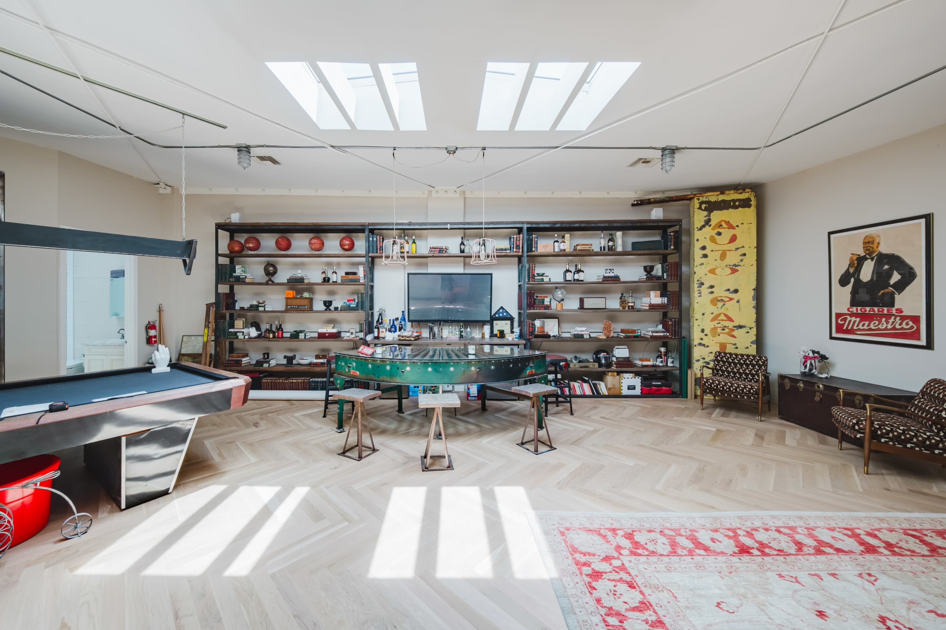 The image shows a spacious room featuring a green piano, a pool table, shelving with various items, and two patterned armchairs.