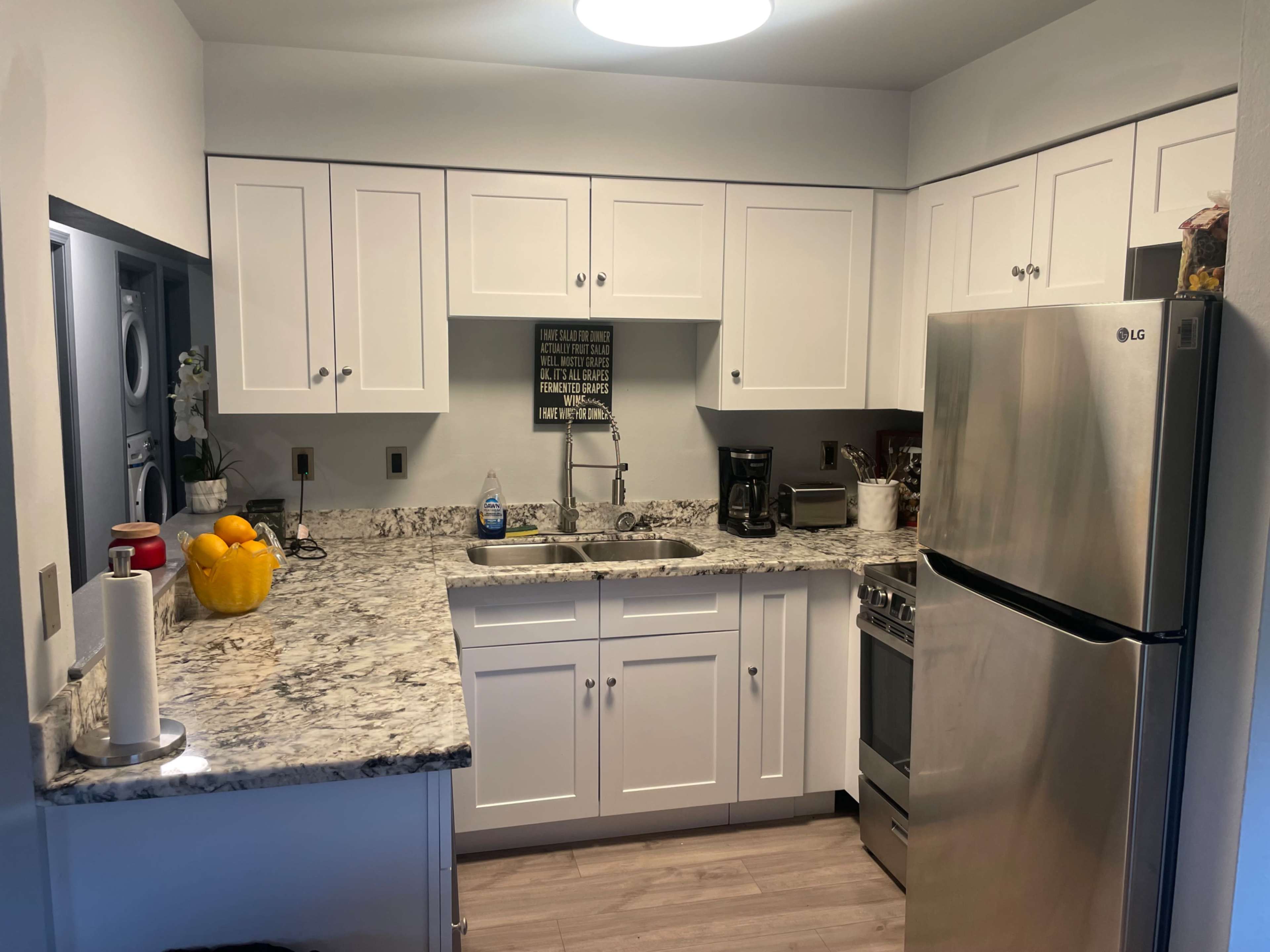 The image shows a modern kitchen with white cabinets, a granite countertop, and stainless steel appliances.