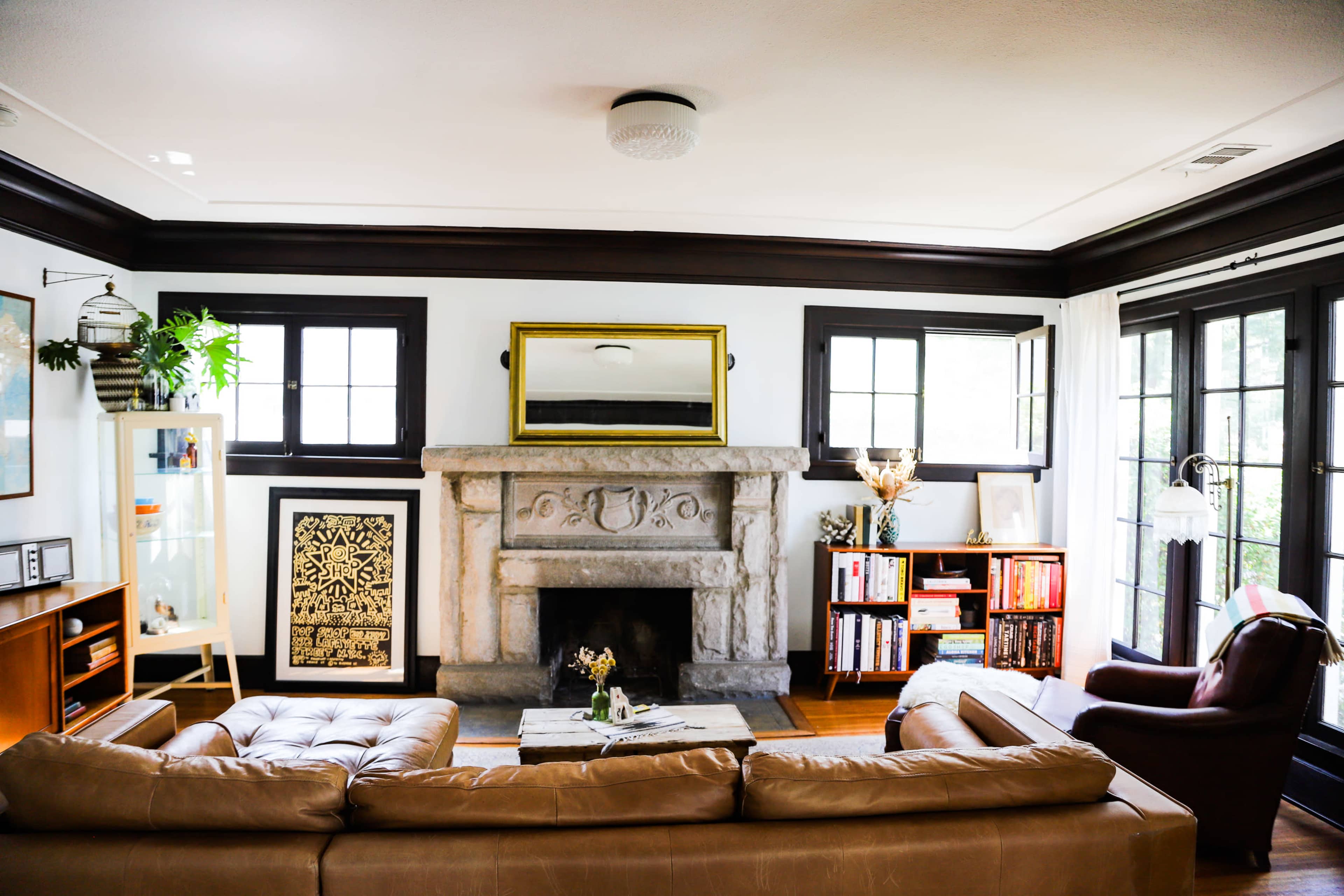 The image shows a cozy living room with a stone fireplace as a focal point, flanked by bookshelves and windows.
