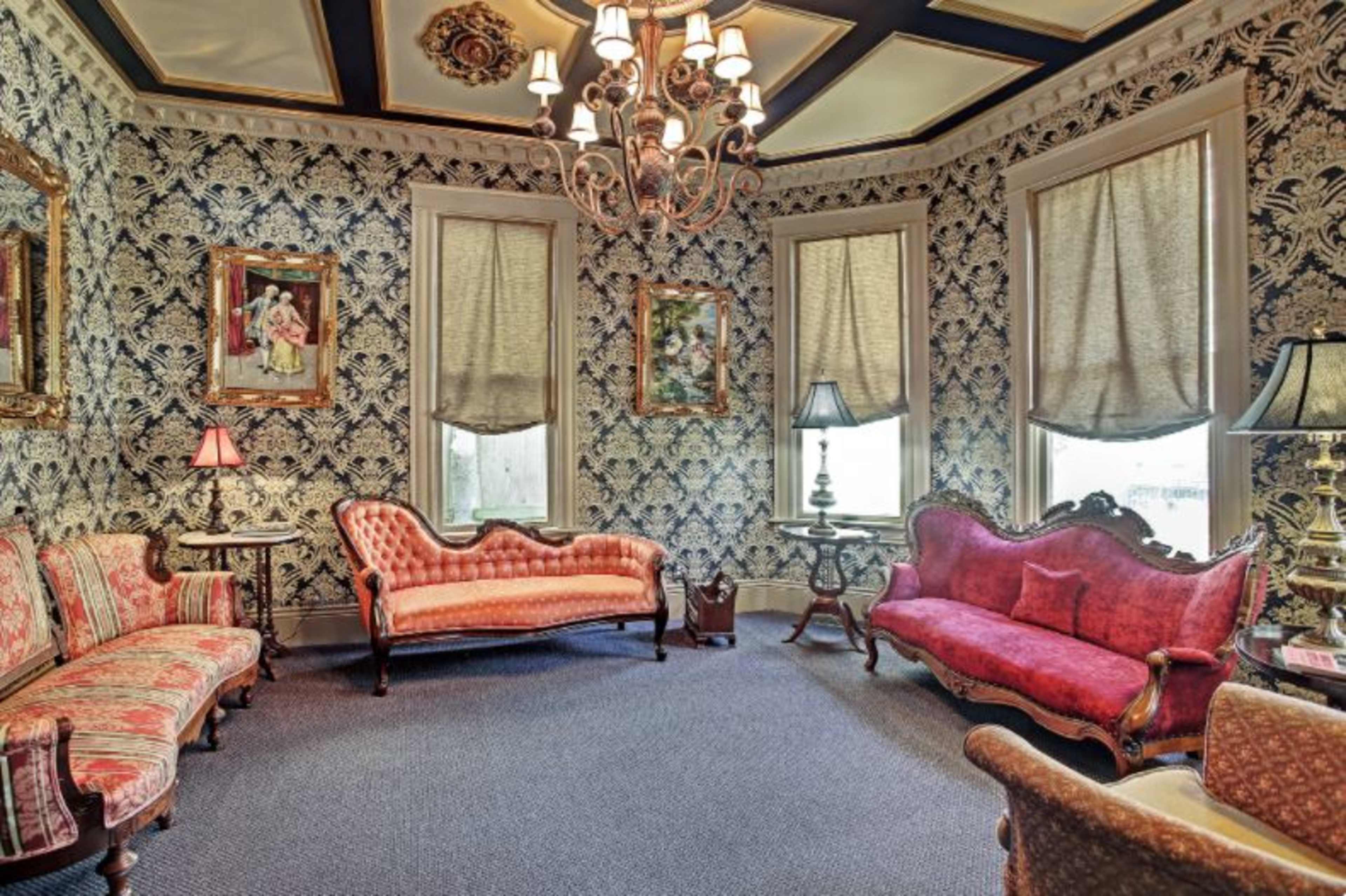 A vintage sitting room with floral wallpaper, two elegant couches, and various lamps providing ambient lighting.