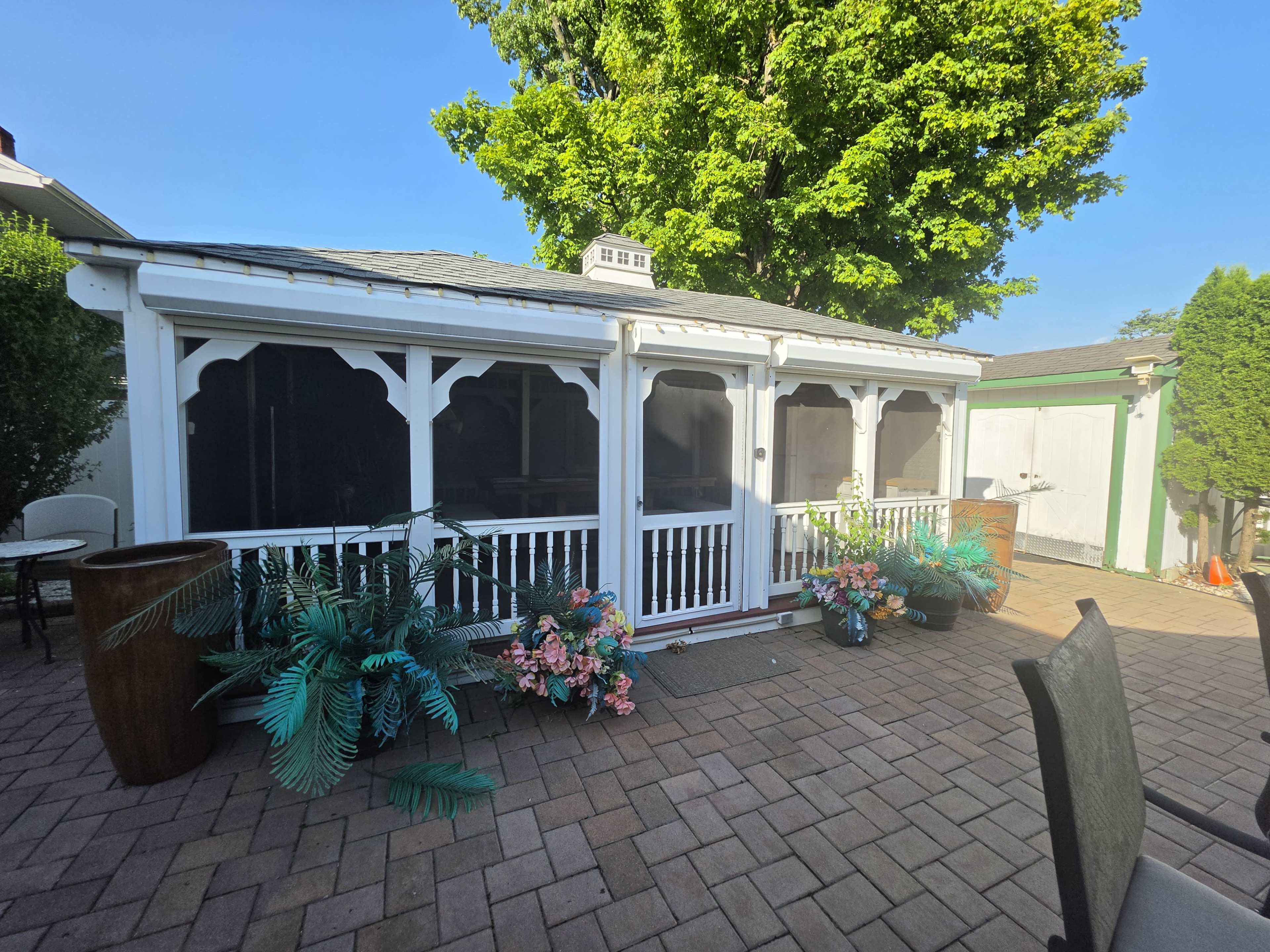 The image shows a screened patio with decorative plants and flowers, situated beside a clear blue sky.