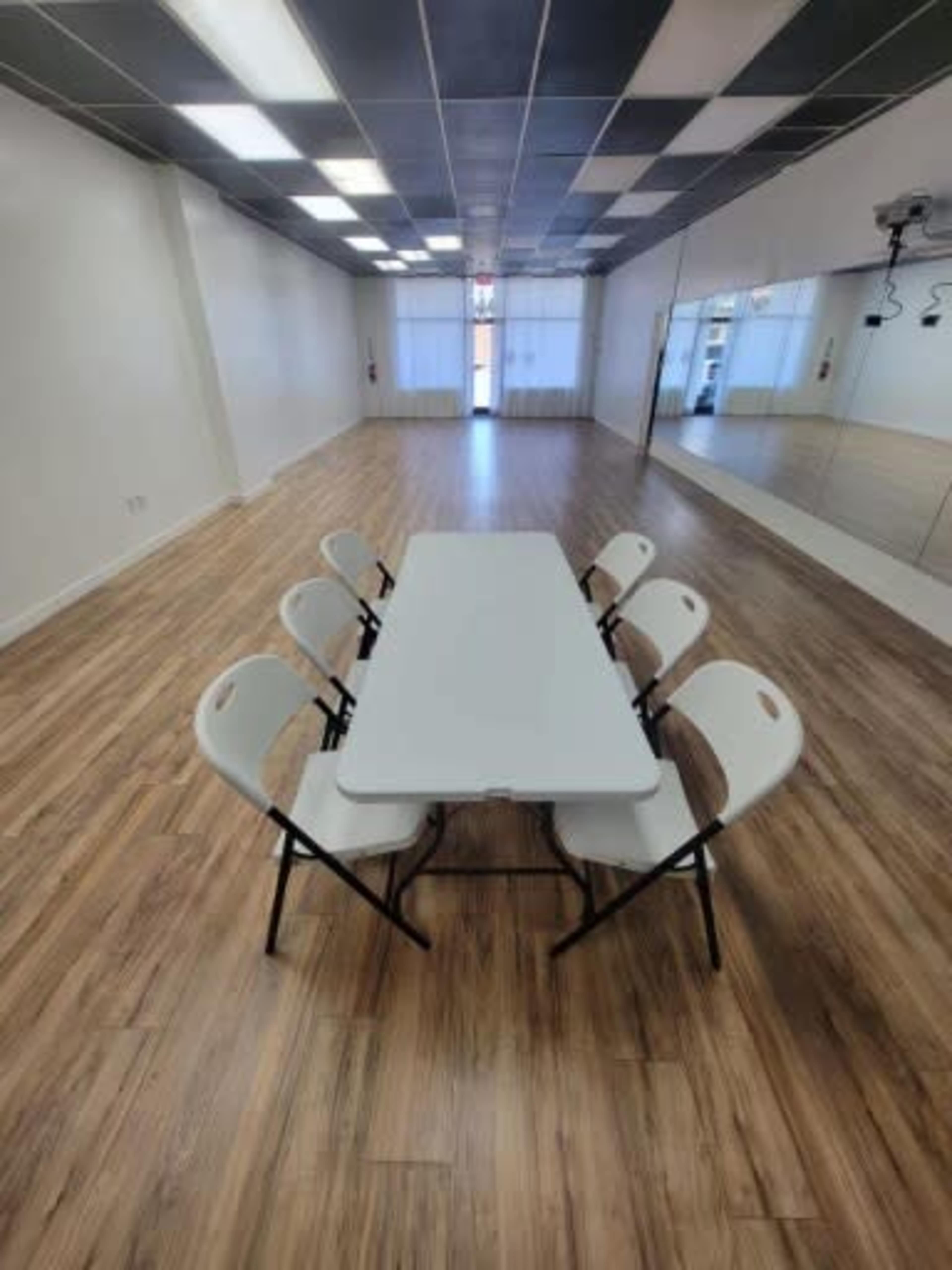 A long white table is set up in the center of a spacious, well-lit room with wooden flooring and a large mirror on one wall.