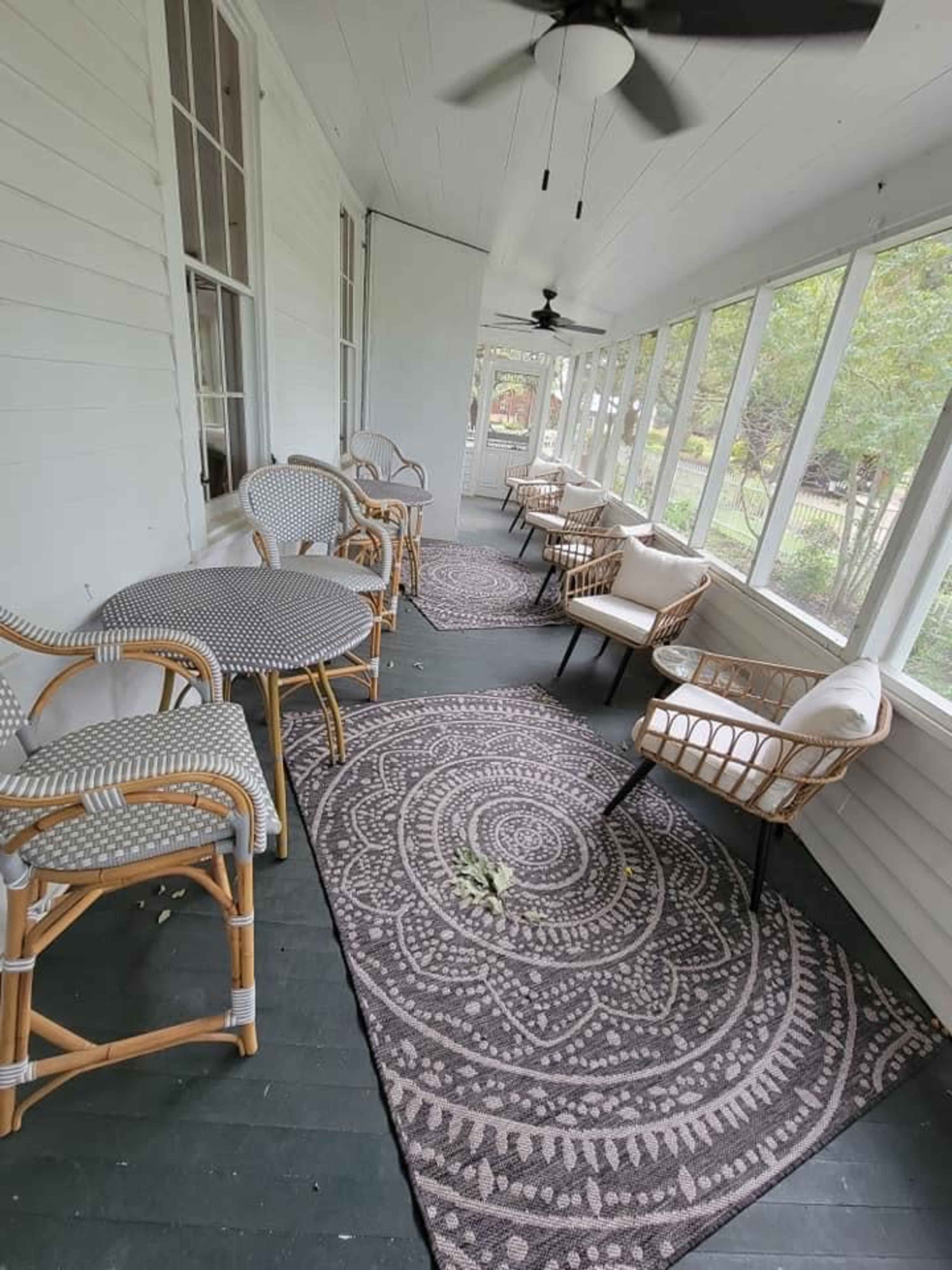 A screened-in porch featuring several rattan chairs and tables arranged on patterned rugs.