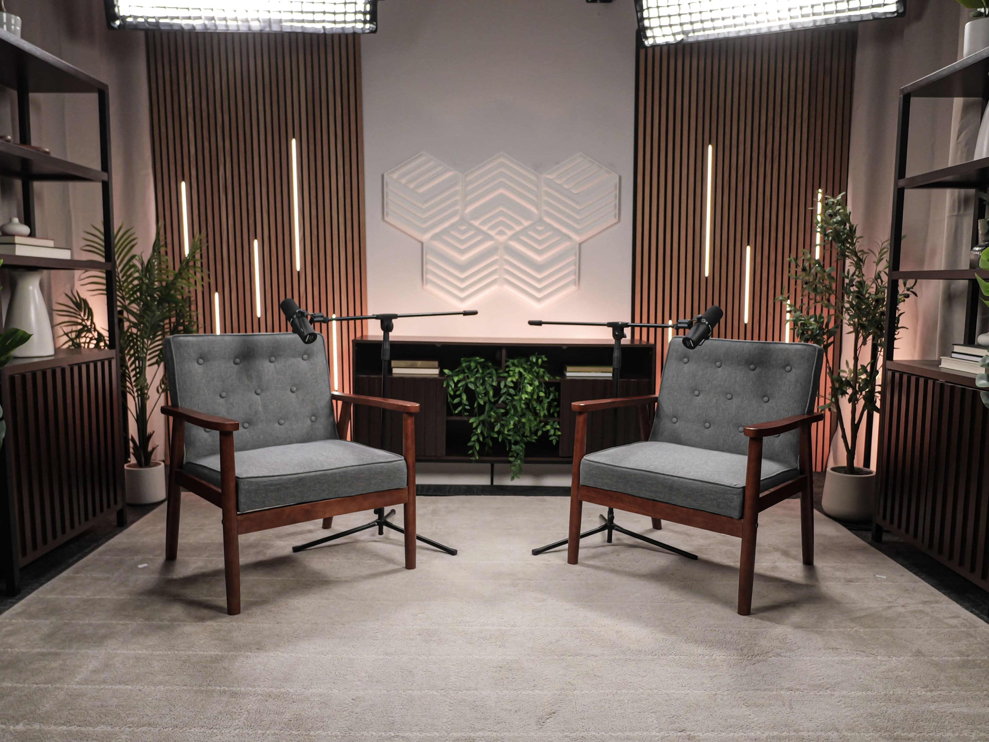 The image shows a studio setting with two upholstered chairs positioned across from each other, a decorative background featuring geometric shapes, and studio lights above.