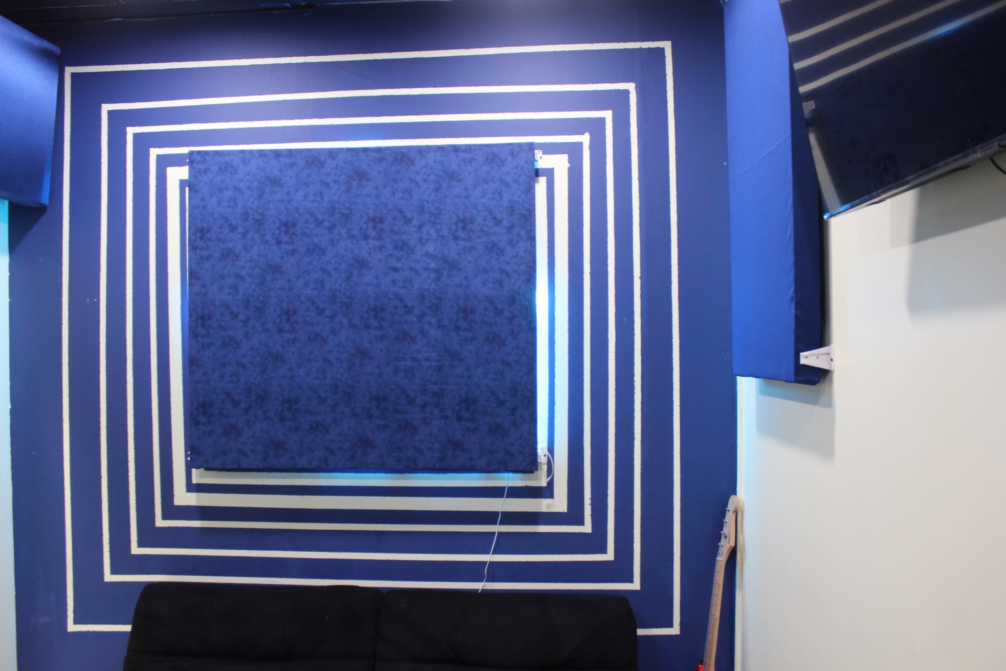The image shows a blue wall with concentric white stripes and a blue curtain in the center, above a black sofa.