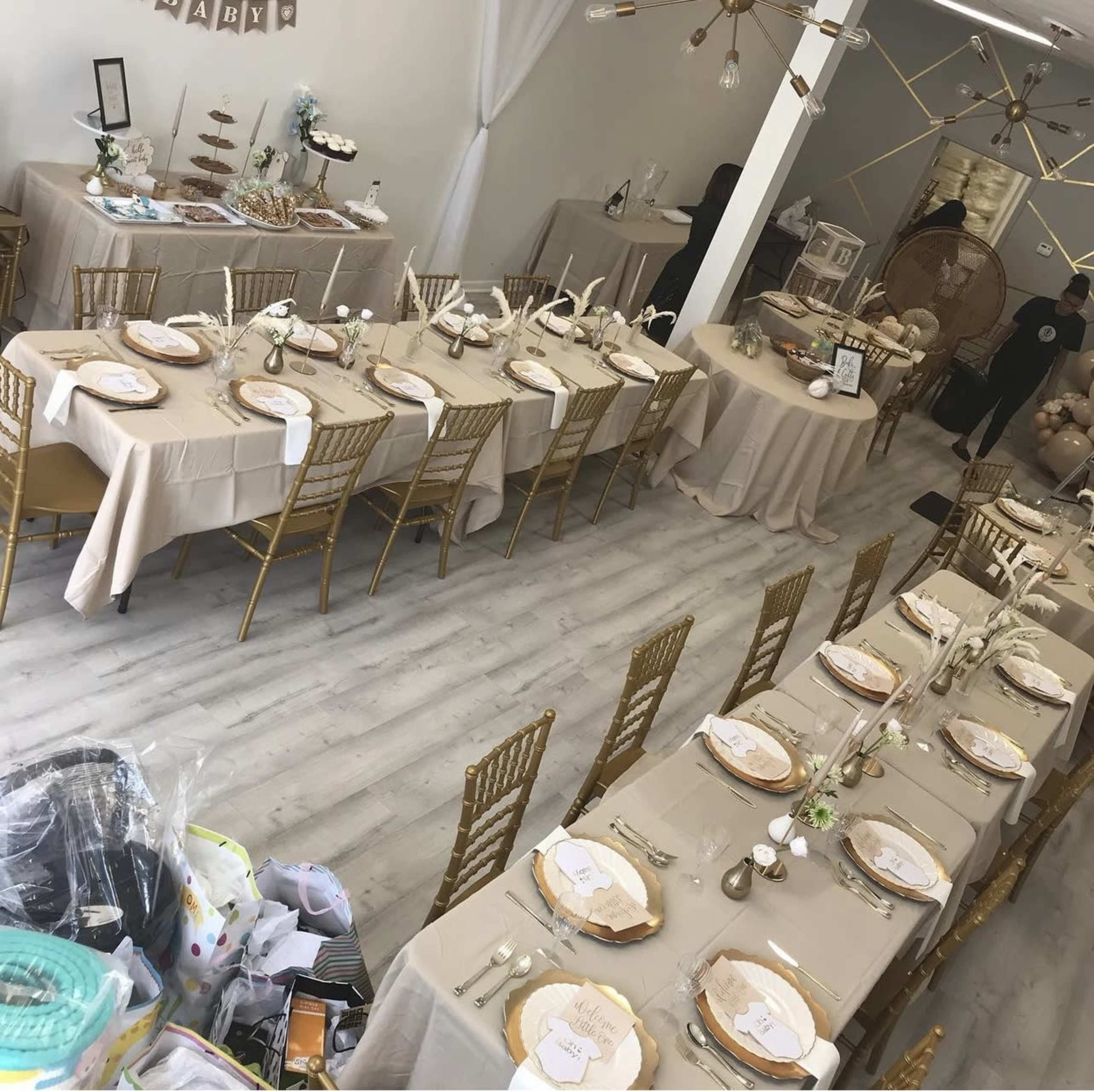 A banquet hall with several elegantly set tables, featuring gold chairs and beige tablecloths, arranged for a special event.