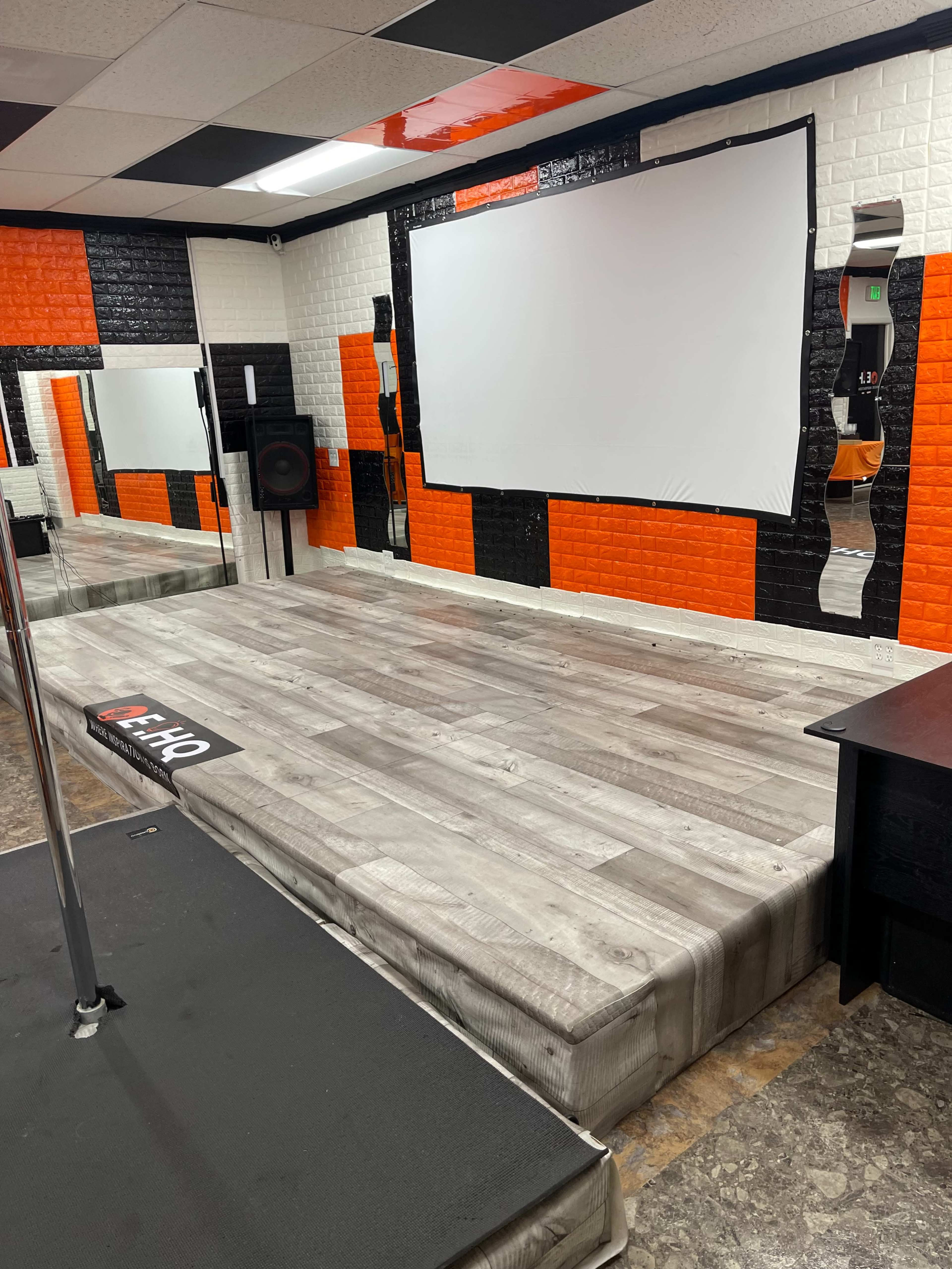 A dance or performance studio with a mirrored wall, a raised wooden stage, and an area for a sound system.