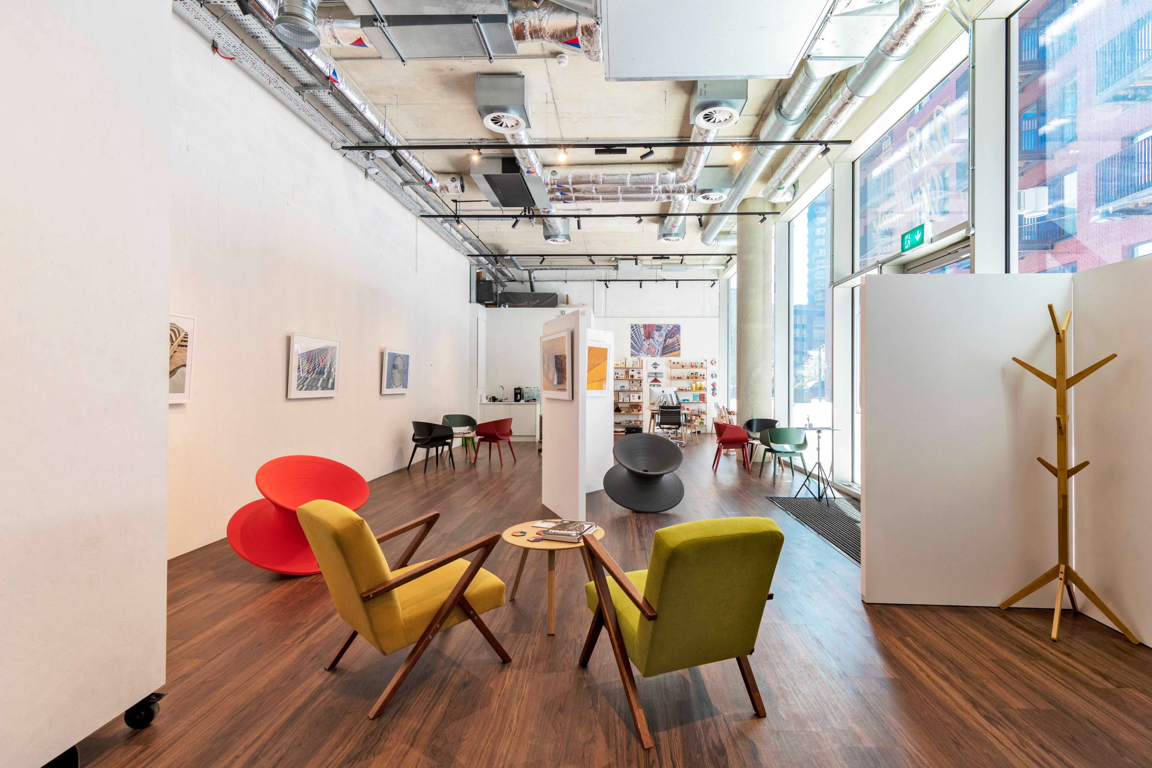 A modern art gallery with a polished wooden floor, displaying various chairs and partitions in an open layout.