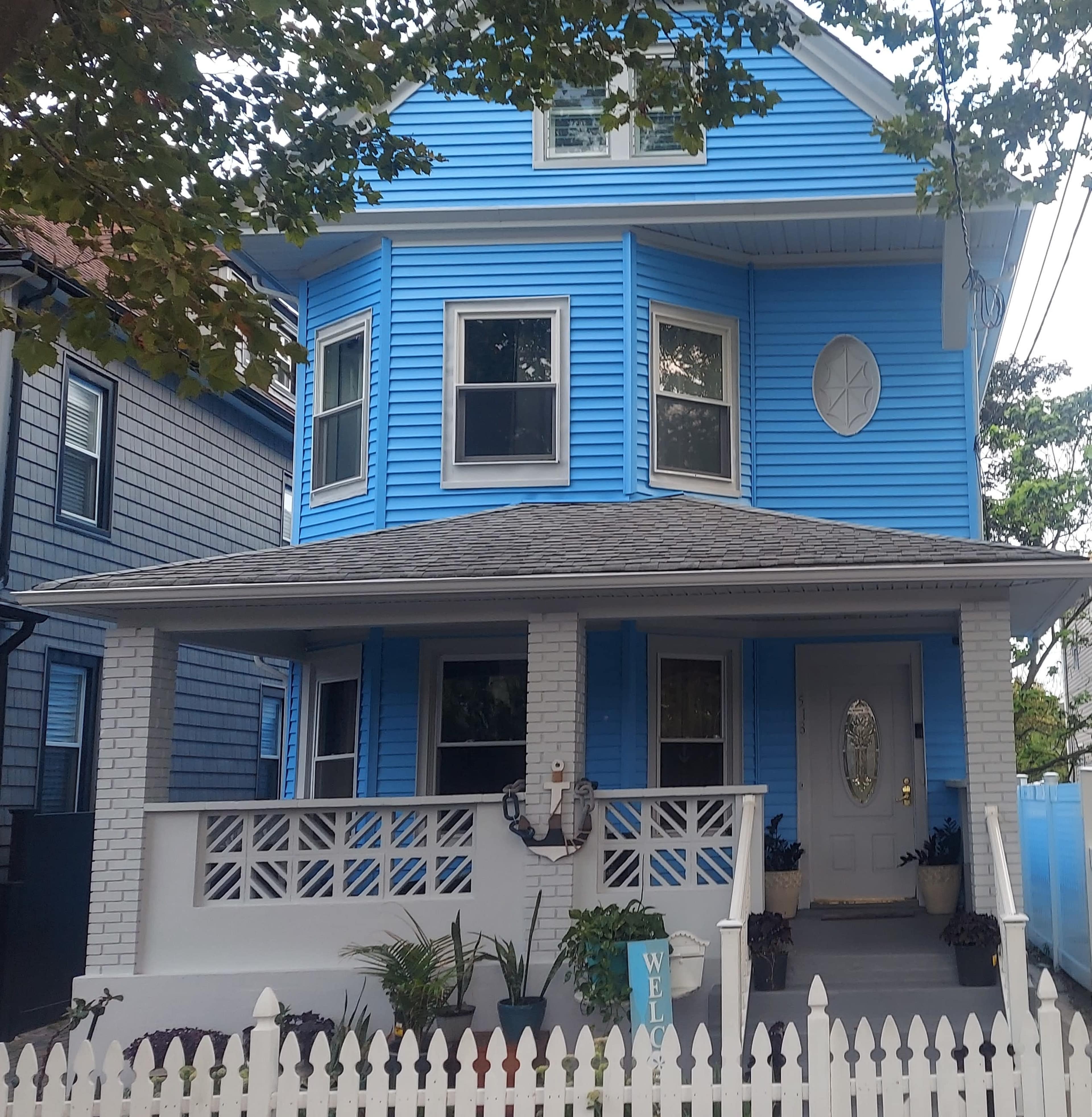 A blue two-story house with a front porch and white picket fence features large windows and a decorative star on the facade.
