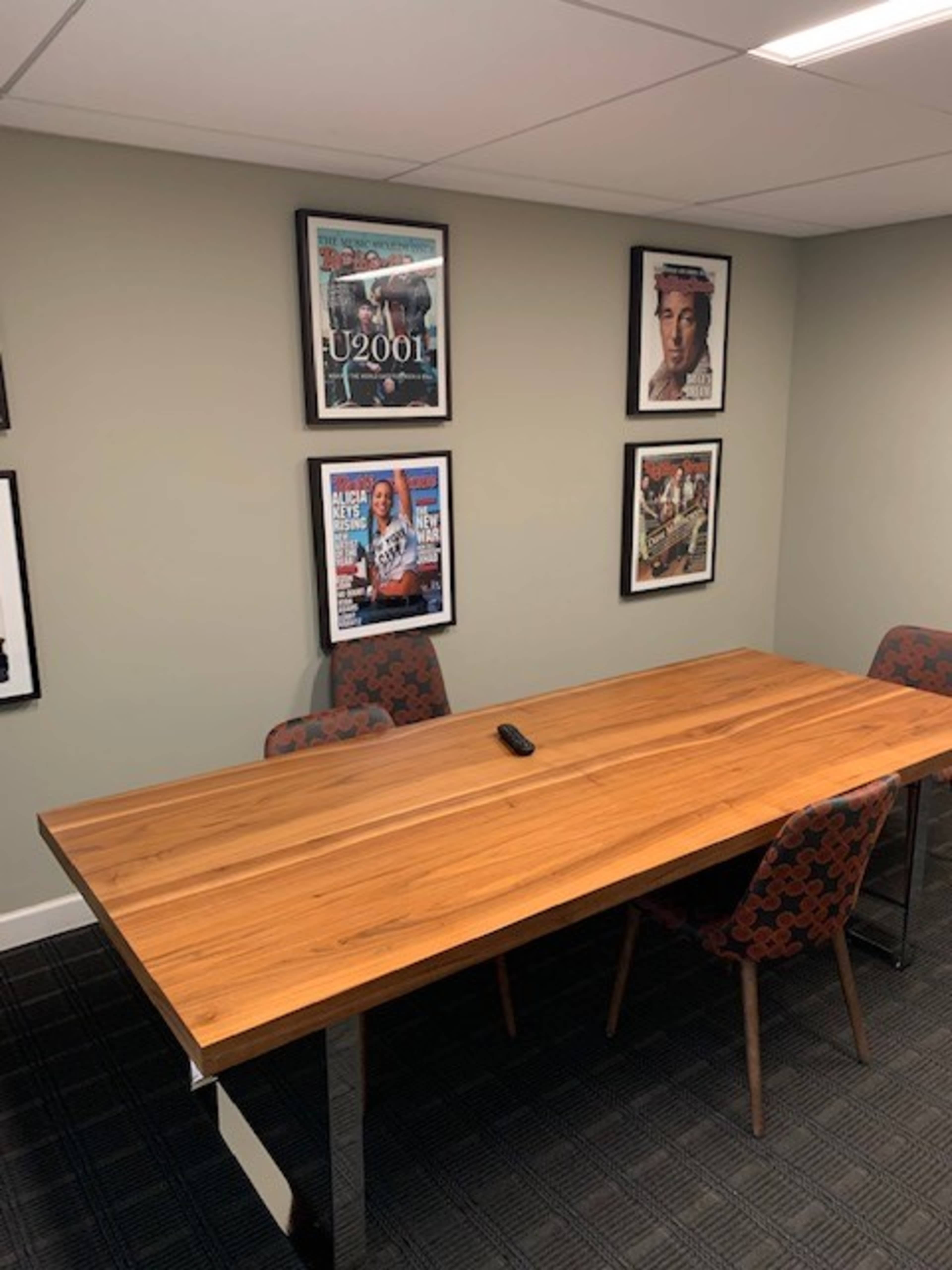 A wooden conference table with metal legs is positioned in a room surrounded by framed magazine covers on the walls.